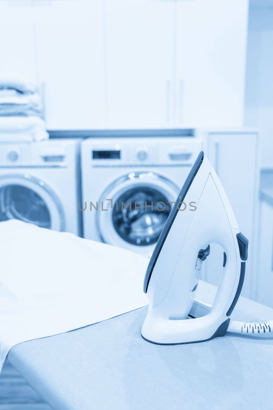 Iron on ironing board with white shirt in modern laundry room