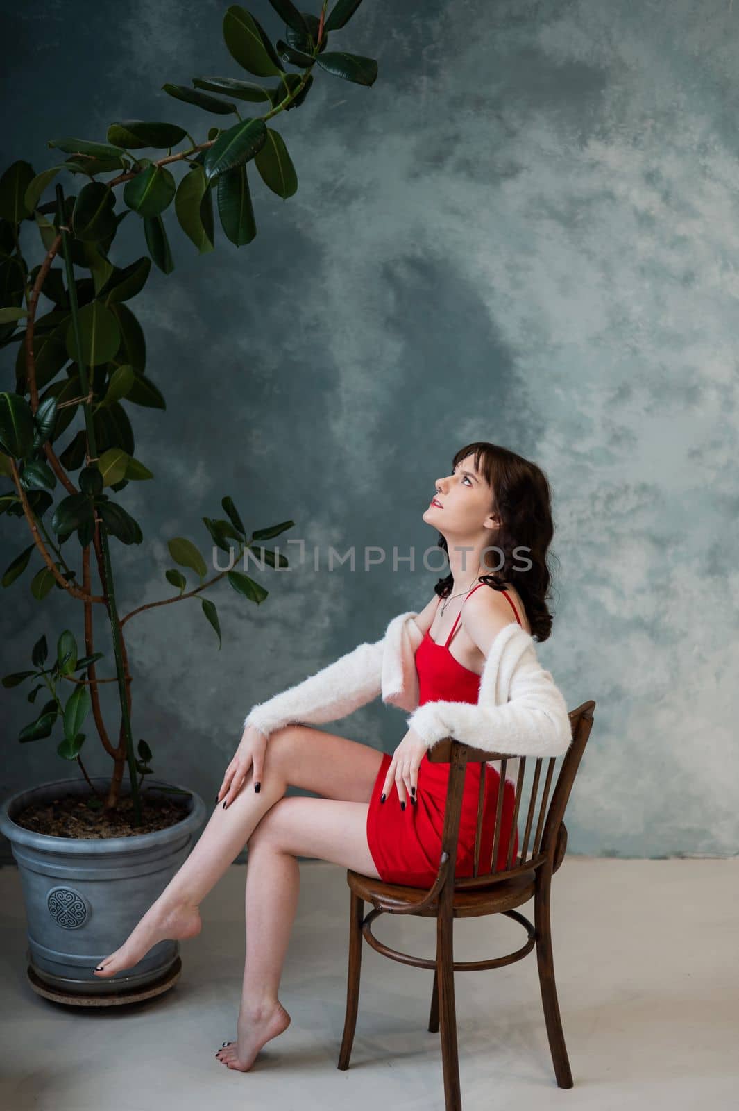 Caucasian brunette woman sits on a wooden chair against a gray wall background