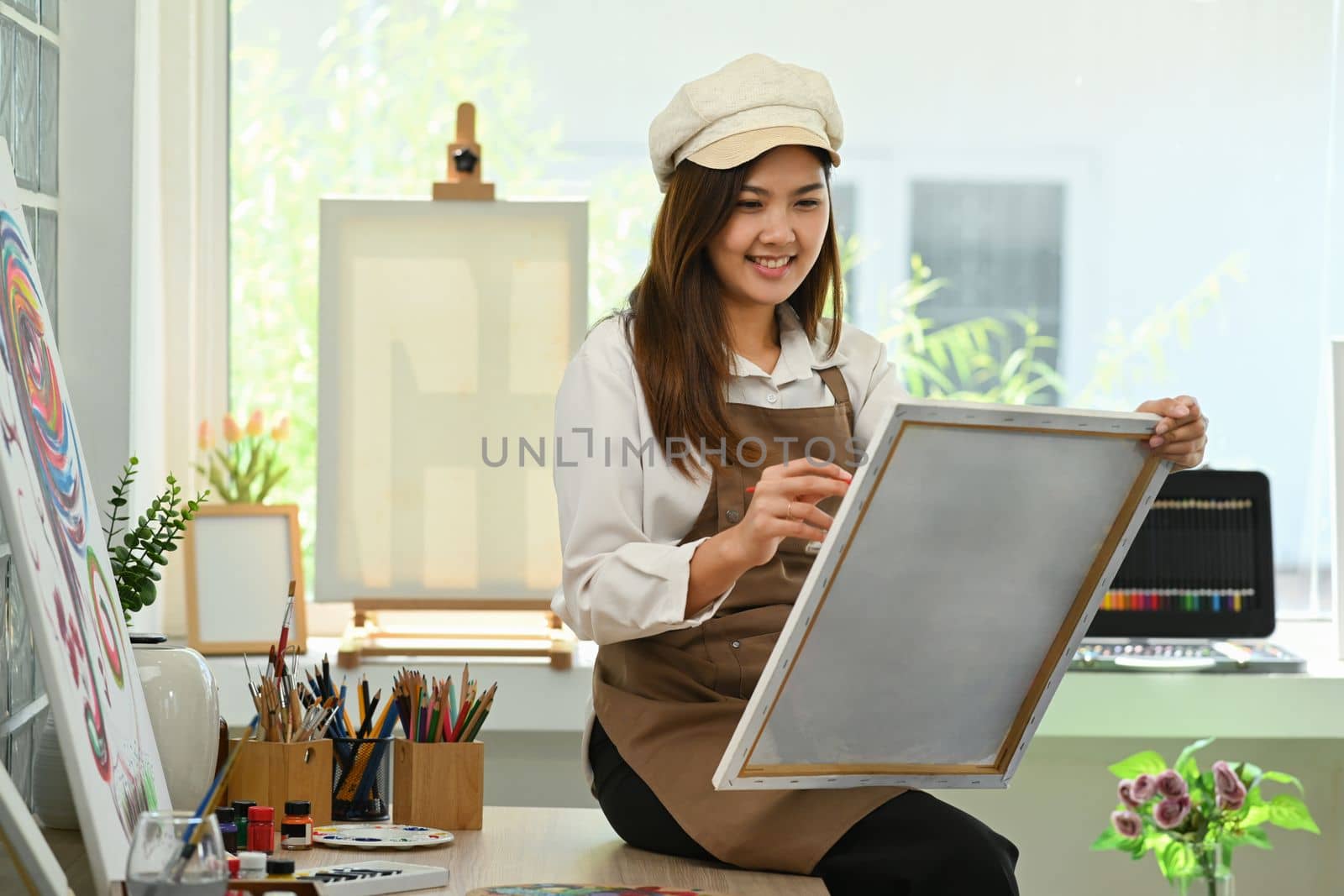 Charming female artist painting on canvas with watercolor in comfortable art studio. Leisure activity, creative hobby and art concept.