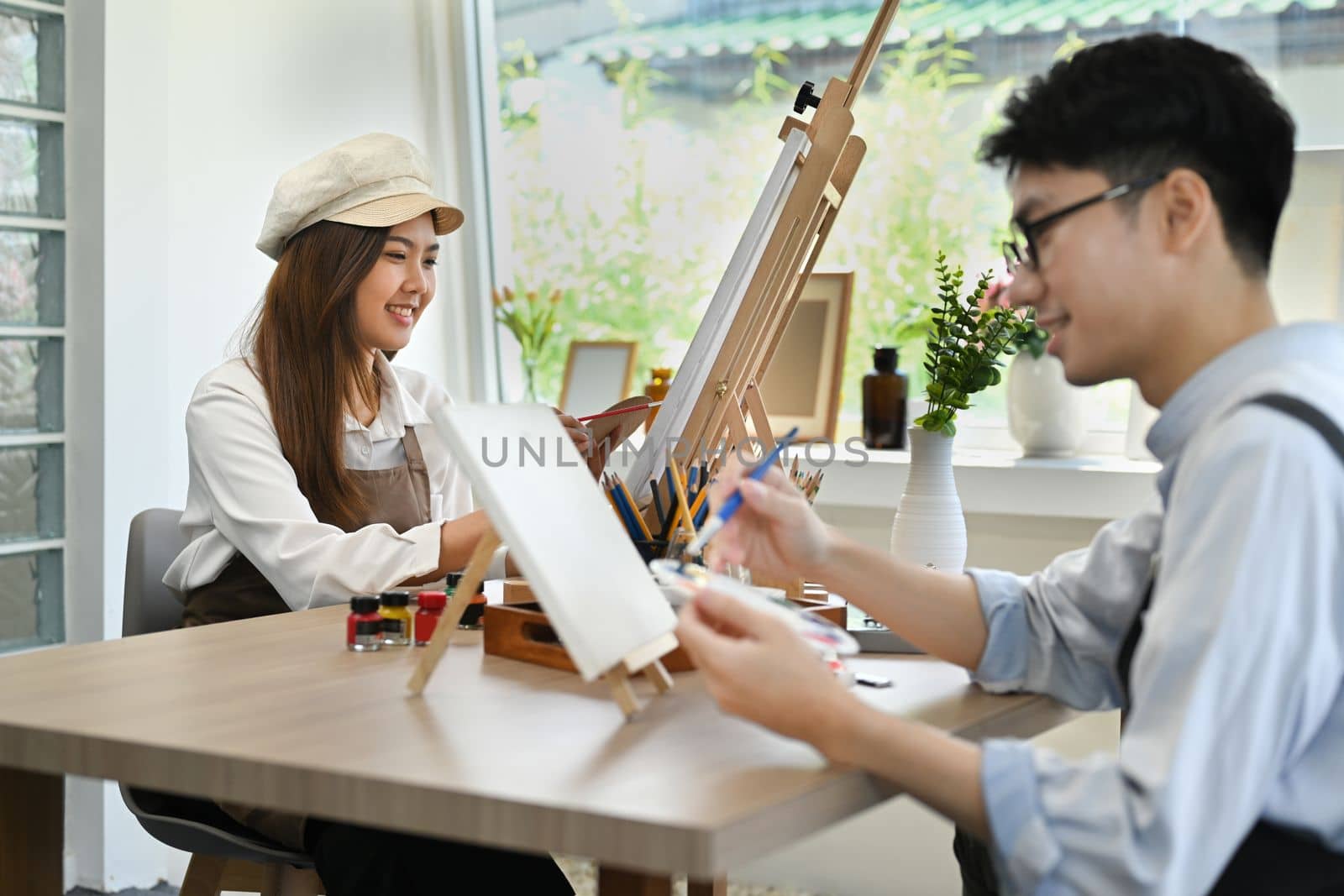 Two young creative people painting picture with watercolor on canvas at art school studio. creativity, education and people concept by prathanchorruangsak