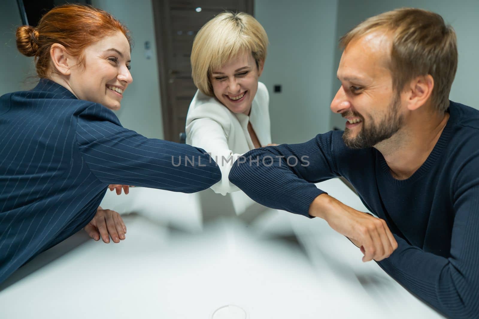 Blond, red-haired woman and bearded man in suits in the office. Business people greet with elbows in the conference room