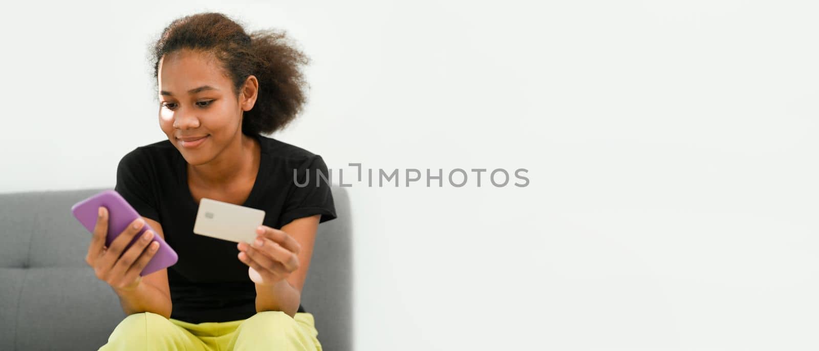 Photo of smiling American African woman holding smart phone and credit card in hand. Panoramic image with empty copy space.