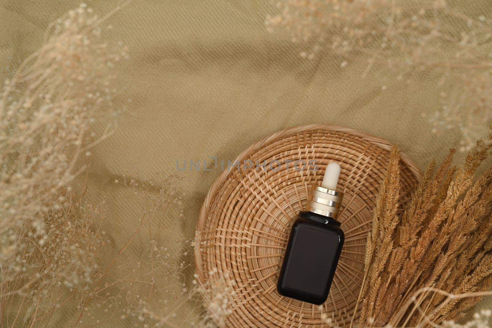 Brown serum dropper bottle on round rattan basket. Skincare beauty products design and branding.