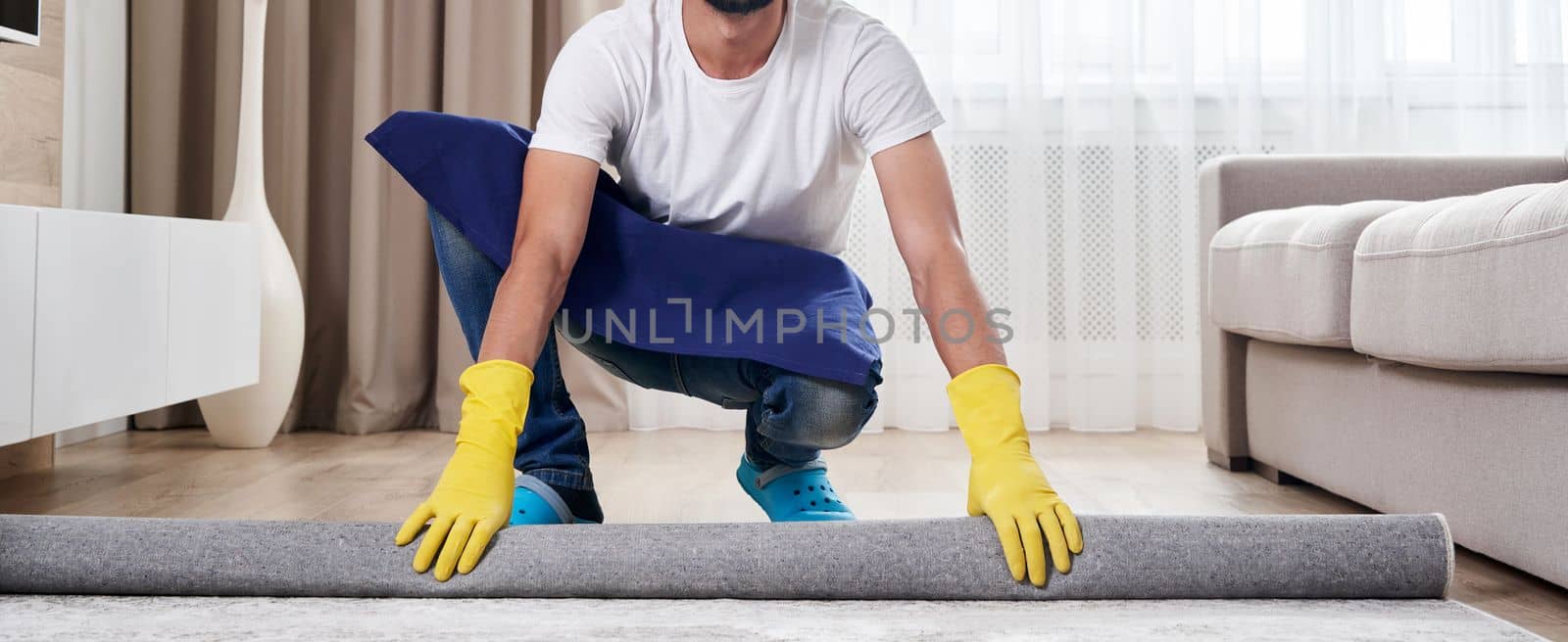 Male Worker In Overalls Rolling Carpet On Floor At Home