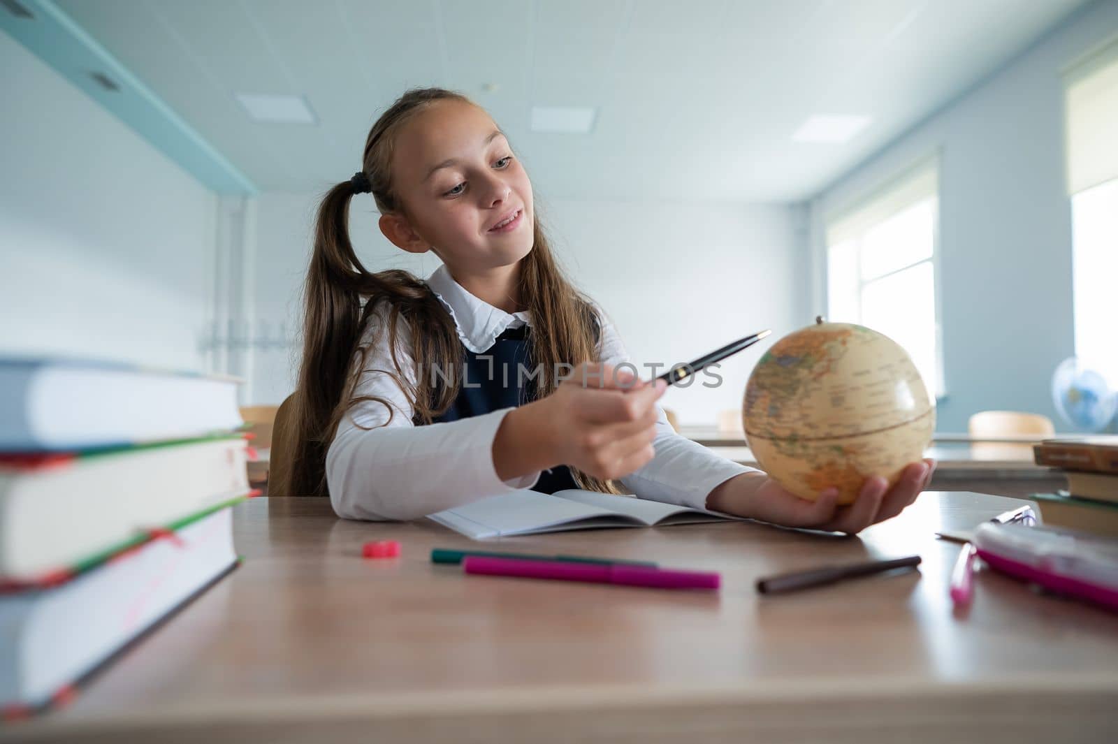 Caucasian schoolgirl sits at her desk at school and studies the globe