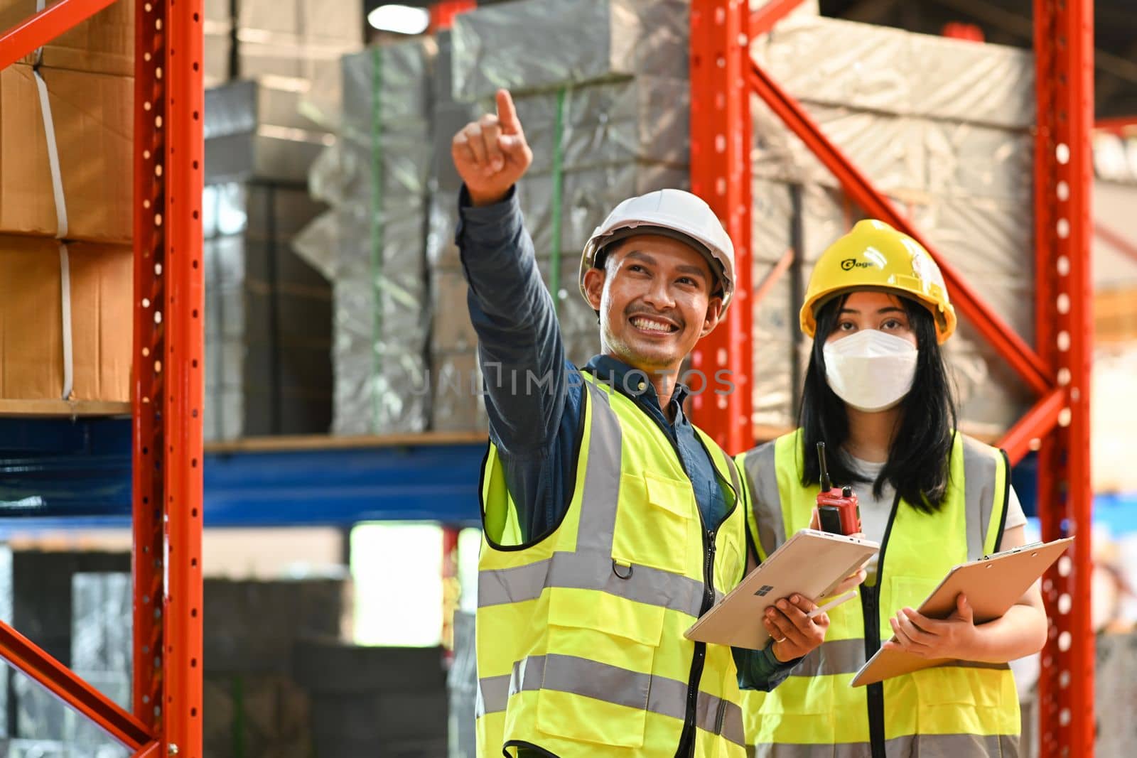 Image of male and female workers wearing hardhats and reflective jacket working together in retail warehouse by prathanchorruangsak