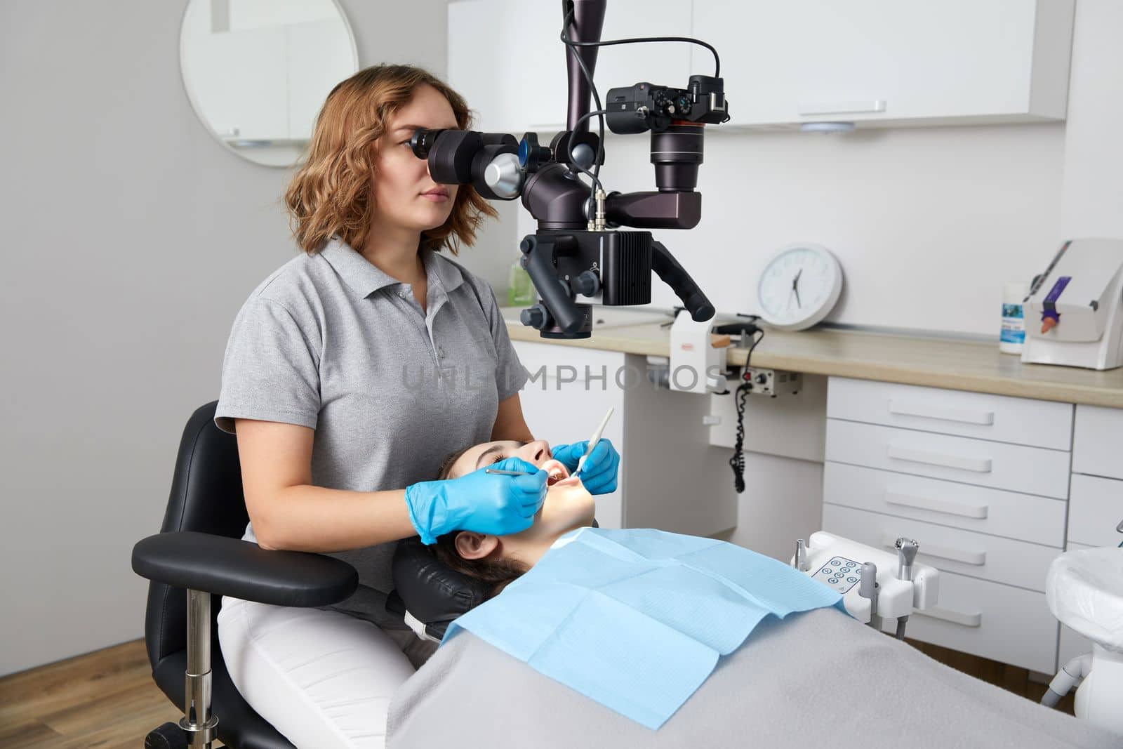 Female dentist with dental tools and microscope treating patient teeth at dental clinic office. Medicine, dentistry and health care concept. by Mariakray