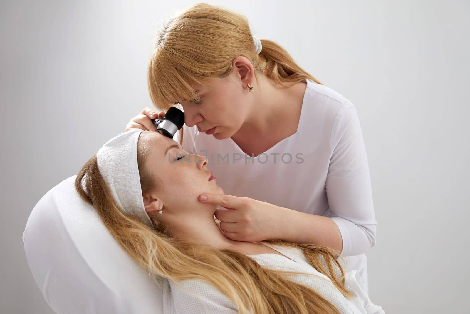 Female doctor looking at patient's skin through magnifying glass. Professional dermatologist and skincare specialist investigating moles or tumor growth signs on wfemale face. Skin checkup concept
