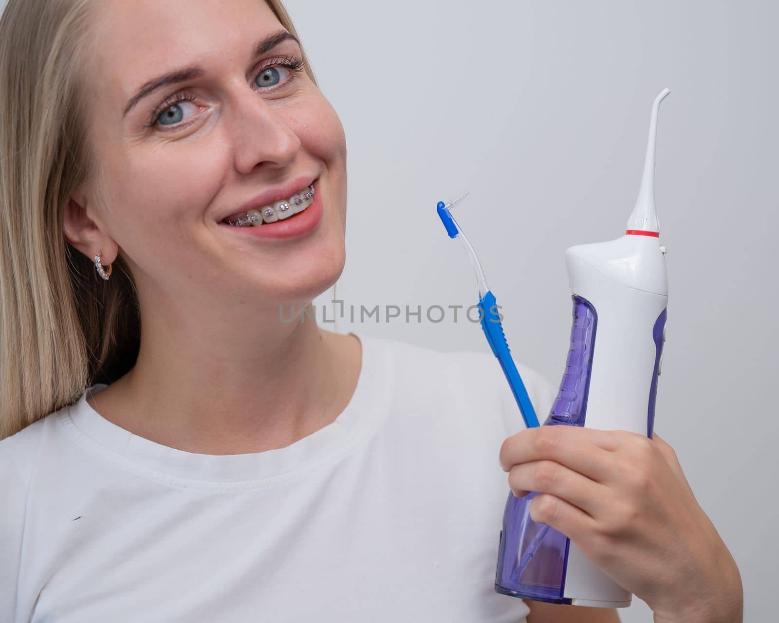 Smiling caucasian woman with braces on her teeth holding an irrigator and a toothbrush