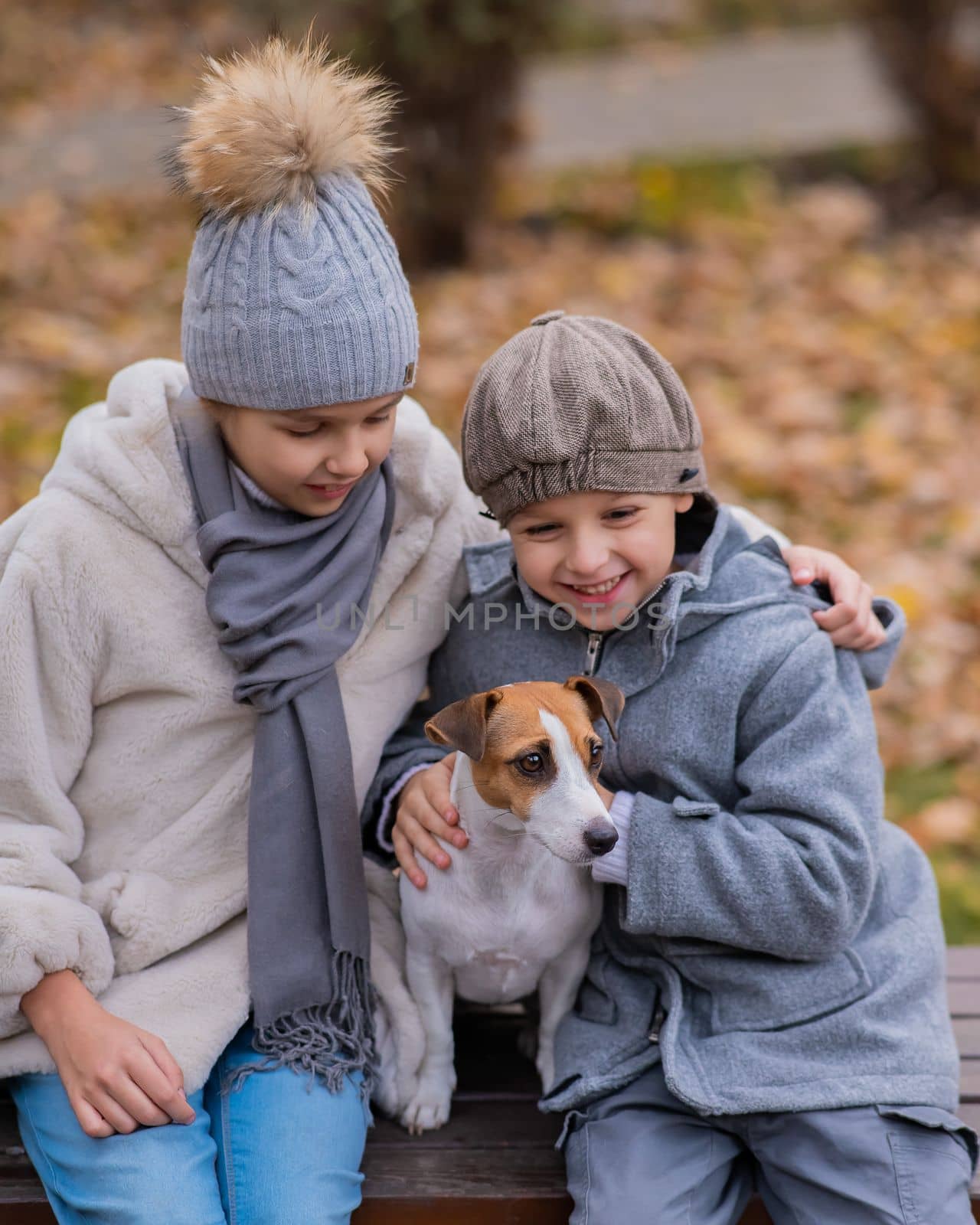 Brother and sister sit in an embrace with a dog on a bench for a walk in the autumn park. Boy, girl and jack russell terrier