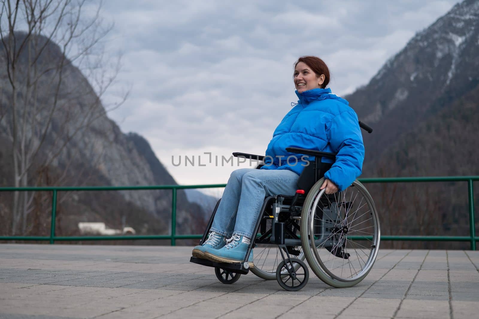 A woman in a wheelchair on a point view admires the high mountains. Thrust to life