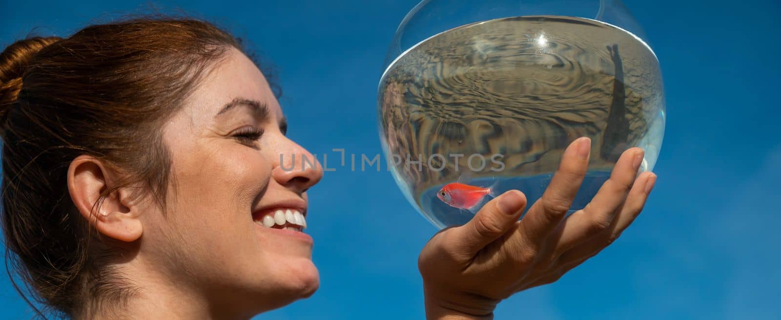 Woman holding round aquarium with goldfish on blue sky background