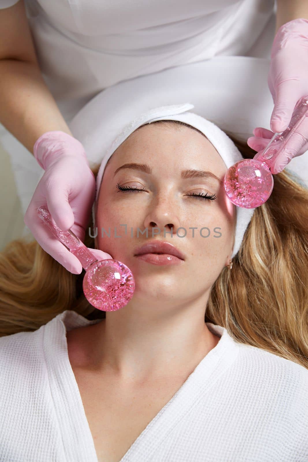 Young woman receiving facial massage with glass balls in beauty salon by Mariakray