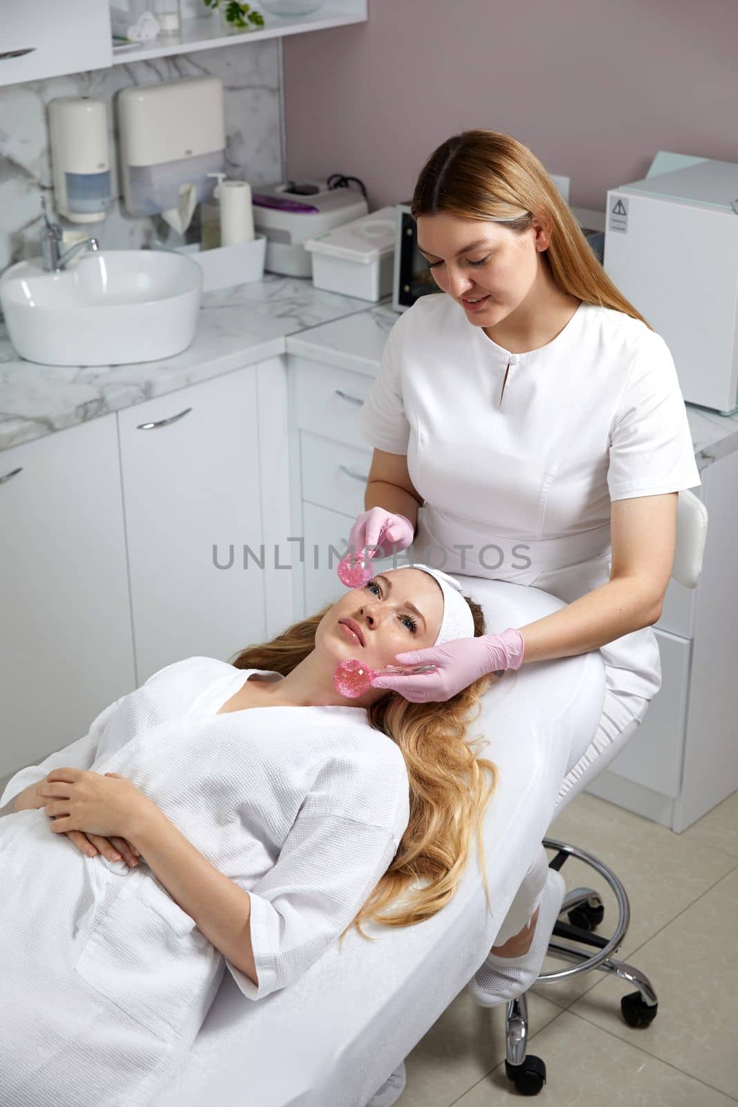 Young woman receiving facial massage with glass balls in beauty salon, concept of face massage in spa