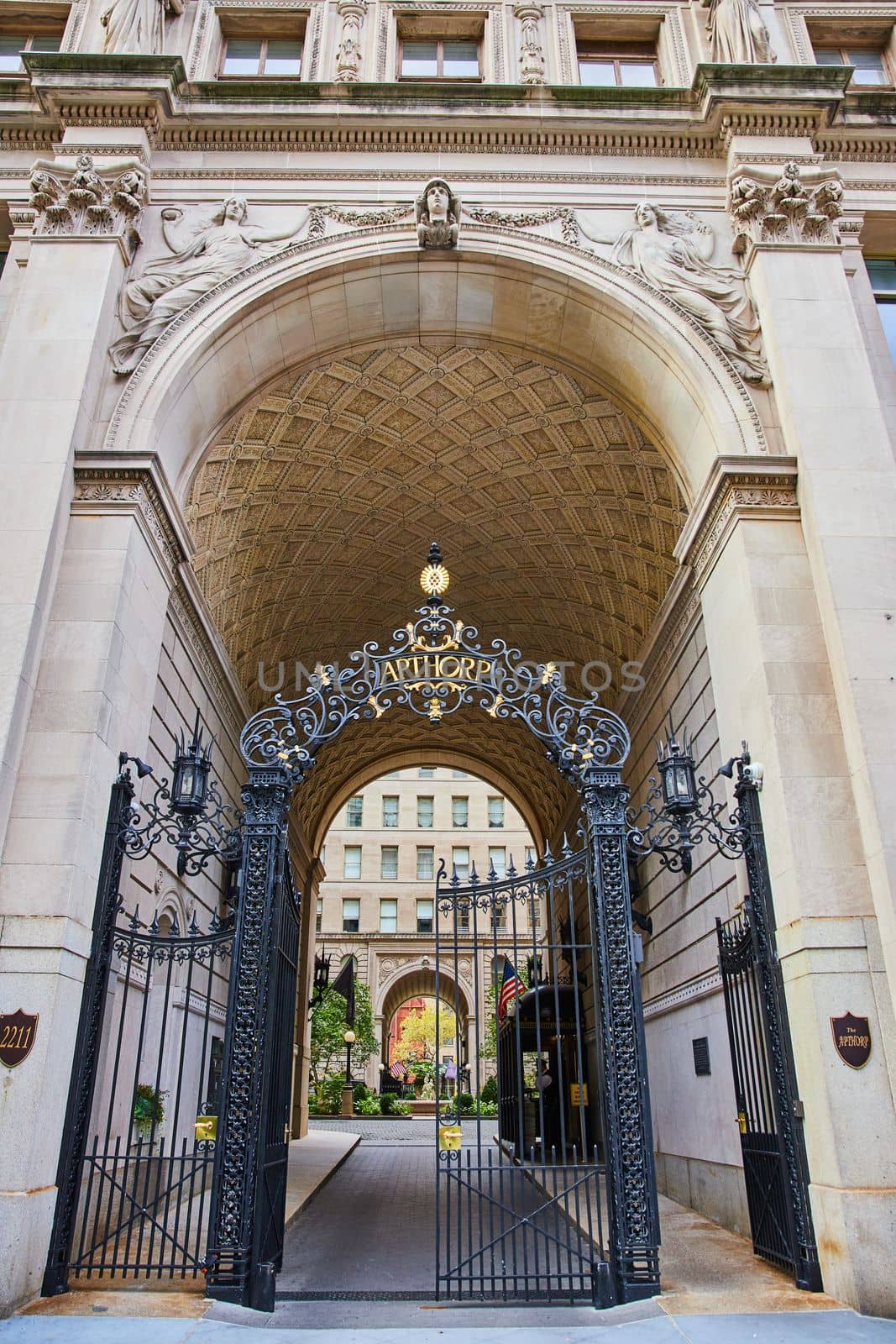 Image of Limestone arch blocked by black steel gates lead into beautiful hidden courtyard in New York City