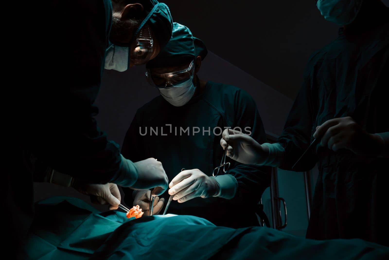 Surgical team performing surgery to patient in sterile operating room. In a surgery room lit by a lamp, a professional and confident surgical team provides medical care to an unconscious patient.