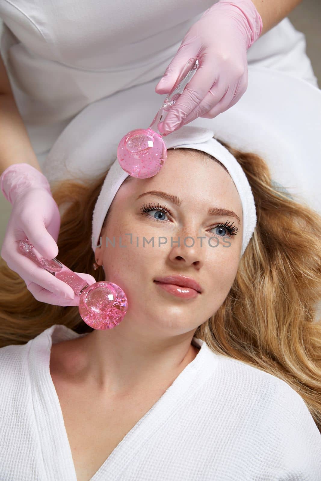 Young woman receiving facial massage with glass balls in beauty salon, concept of face massage in spa
