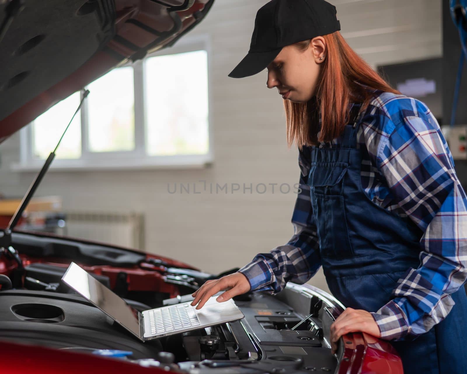 Woman auto mechanic doing engine diagnostics using laptop