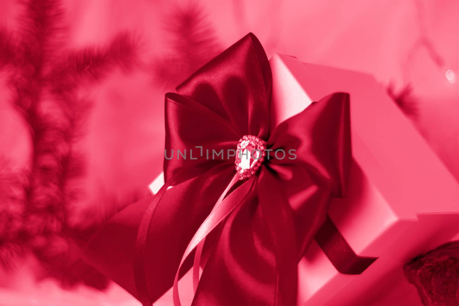 A Christmas gift decorated with a beautiful bow on a light background with a fir twig. Gifts, joy, surprise. Selective focus. the concept of Christmas and New Year. Viva Magenta Background color