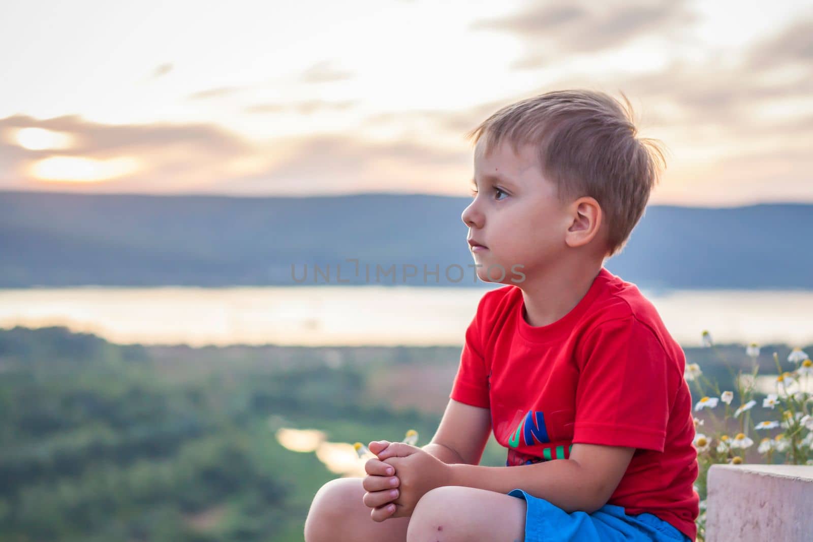Cute Boy in a red T-shirt on the background of a stunning sunset. Journey.  The face expresses natural joyful emotions. Not staged photos from nature. by Alina_Lebed