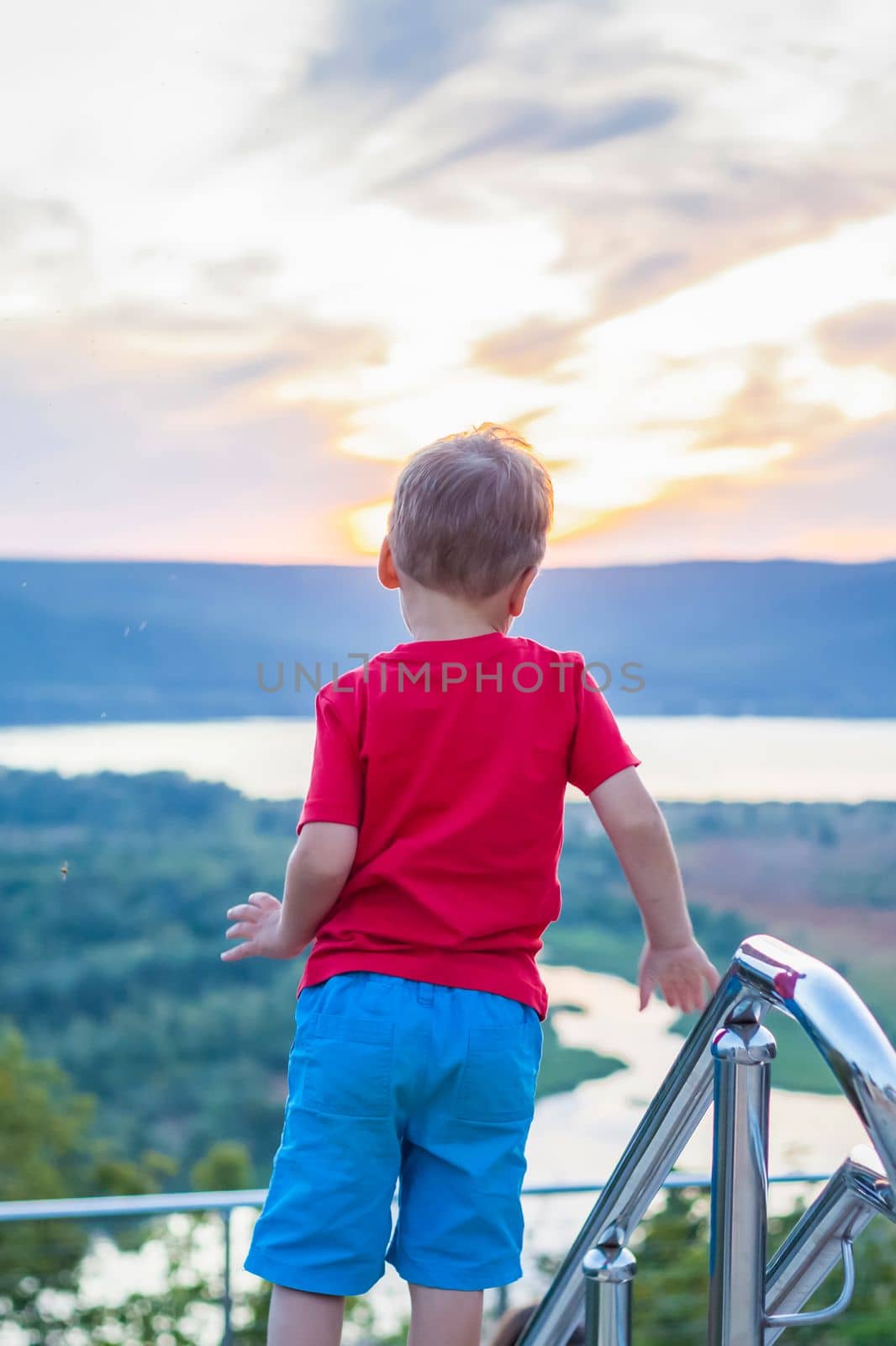 Cute Boy in a red T-shirt on the background of a stunning sunset. Journey.  The face expresses natural joyful emotions. Not staged photos from nature.