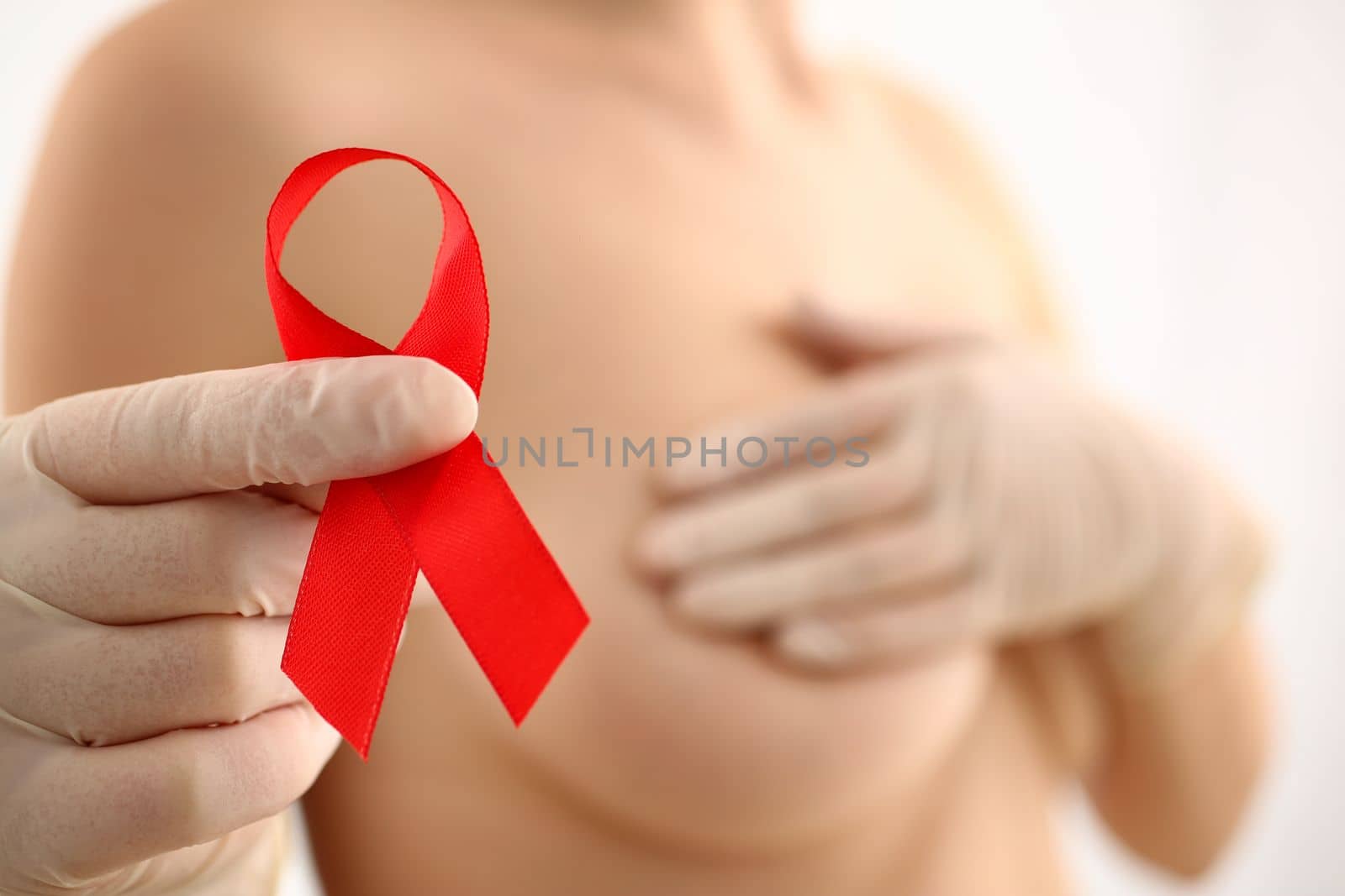 Woman with naked beautiful breasts holds red ribbon. Breast cancer concept