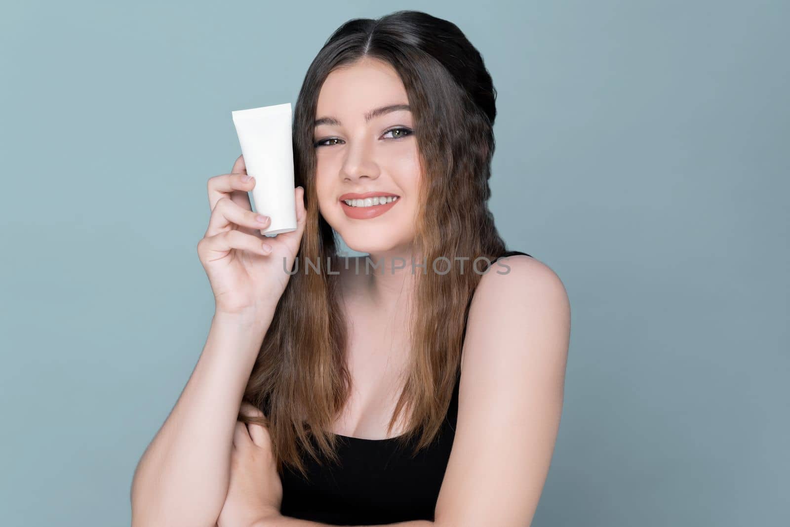 Young charming girl hold mockup moisturizer skincare cream tube or container for copyspace advertising. Photo of beautiful and attractive girl with perfect makeup for beauty concept.