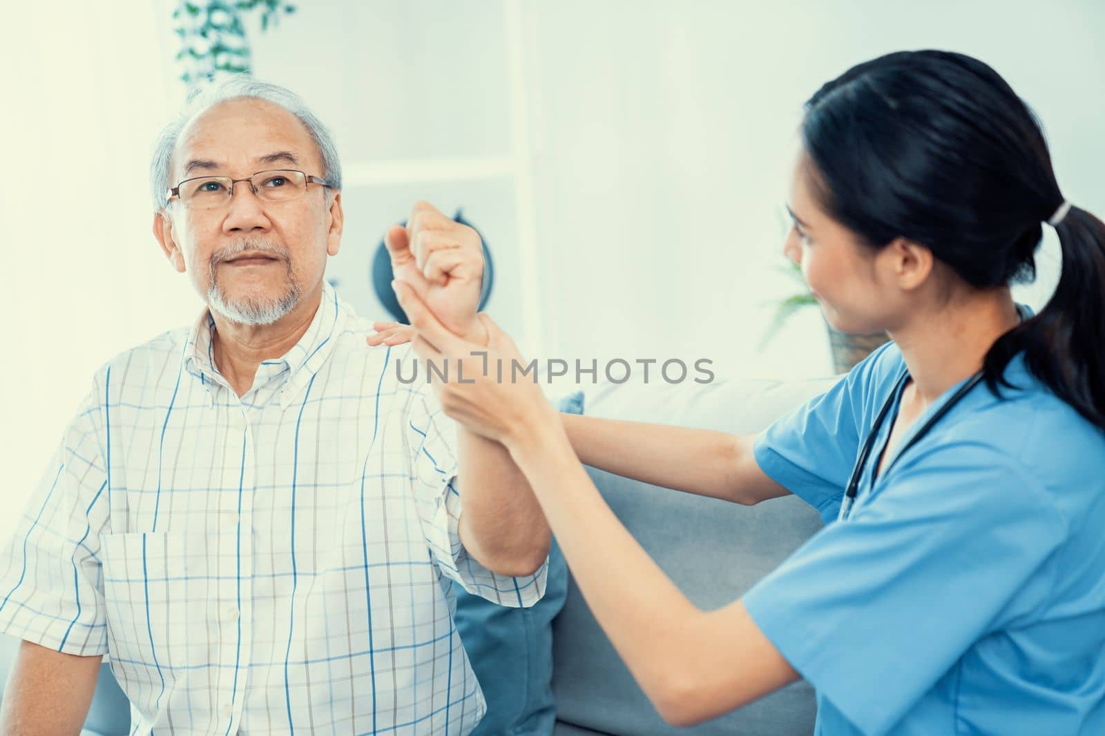 Caring young female doctor performing osteopathy treatment for a contented senior patient. At-home medical treatment for an Asian senior patient, joint pain treatment, medical service for seniors.