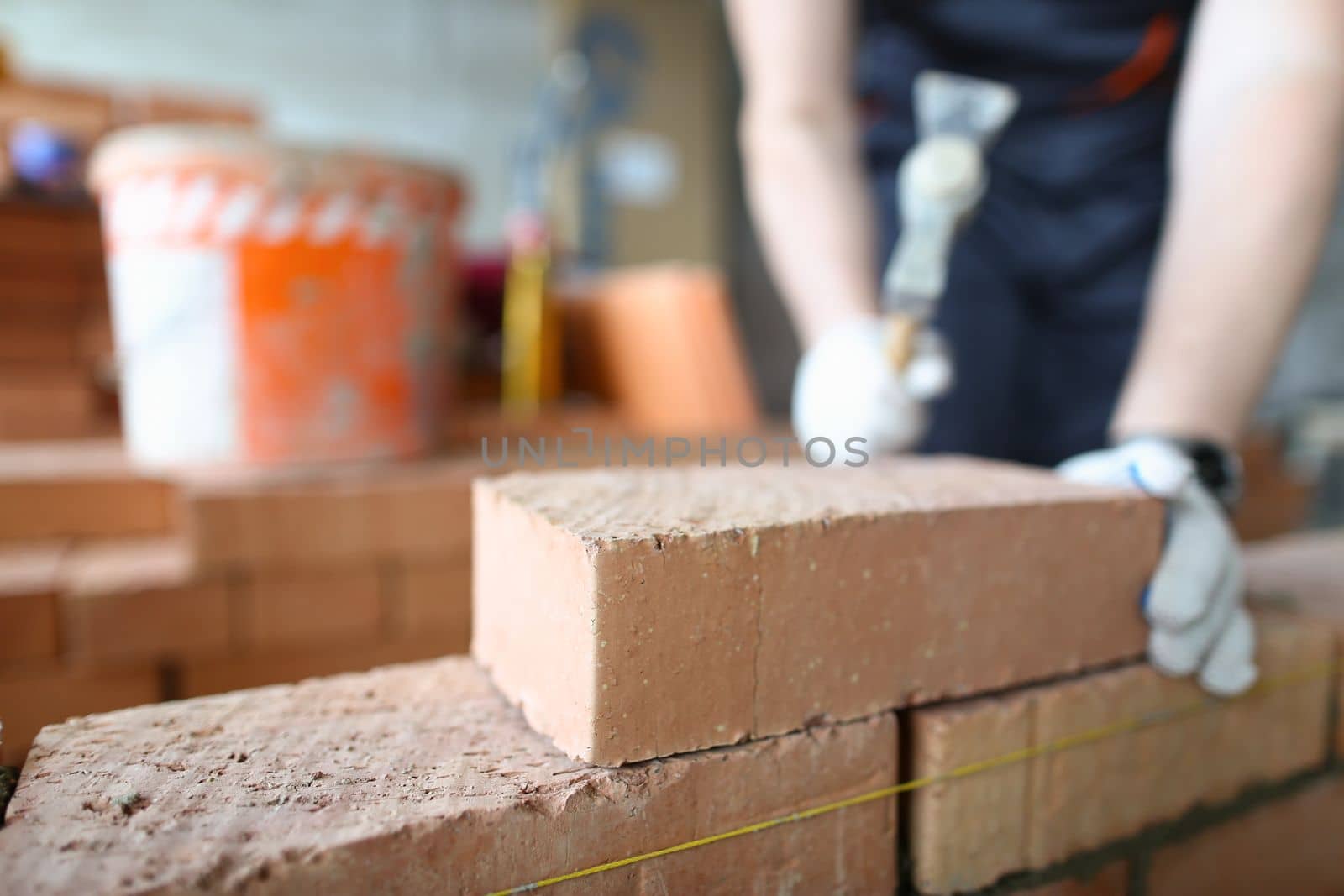 Brick orange wall set laying inside partition room at construction site. Construction worker ironing brick concept