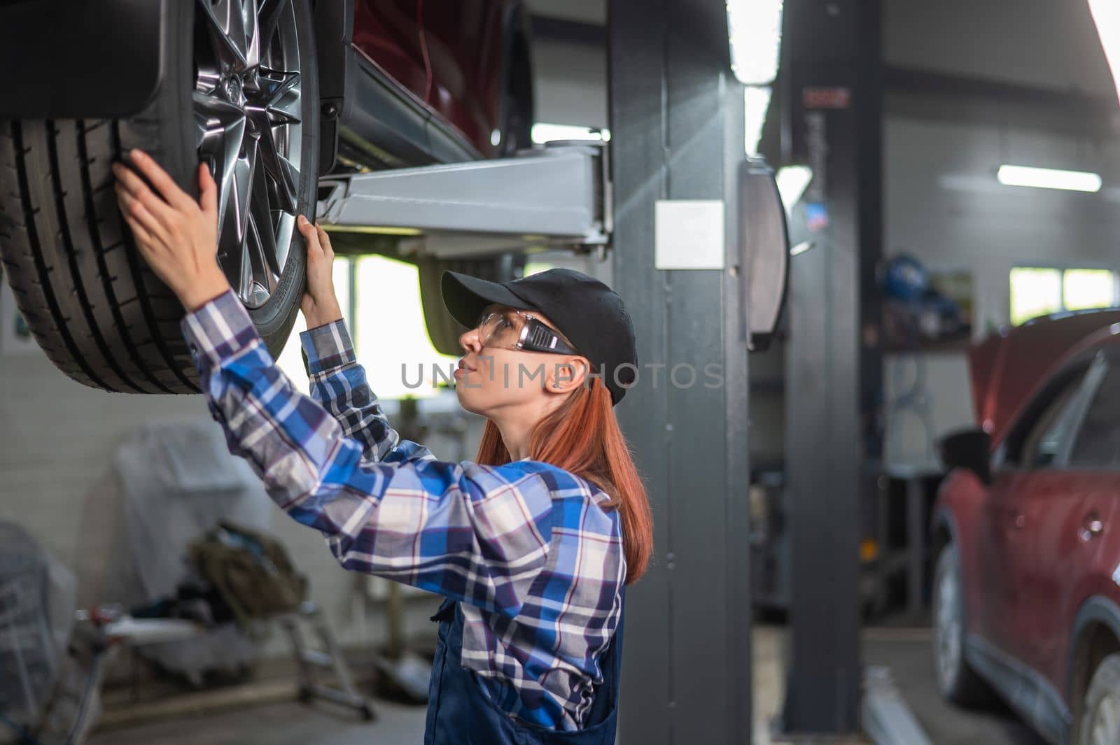 Female mechanic adjusting the tire of the car that is on the lift. A girl at a man's work
