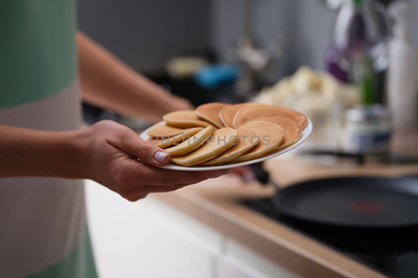 Woman holds plate with fresh delicious pancakes in kitchen. Making pancakes at home concept