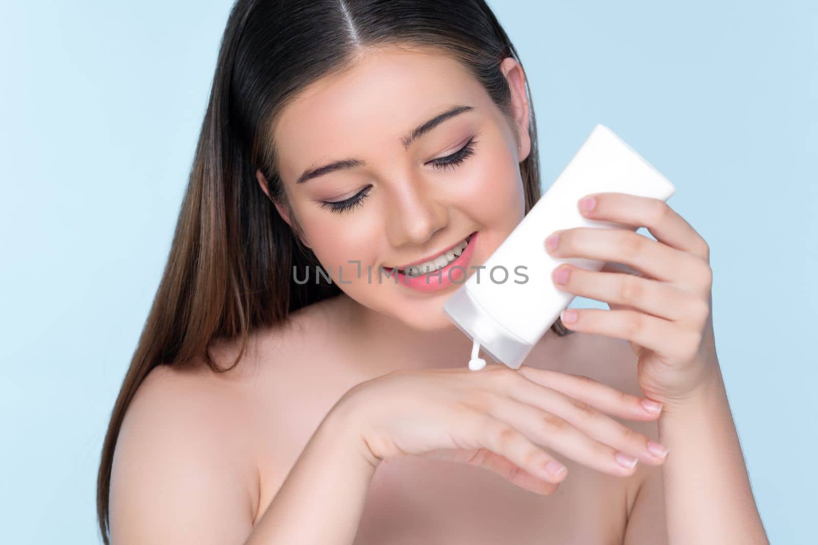 Young charming girl with natural beauty, perfect smooth skin hold lotion, cream, moisturizer tube. Beautiful girl show skincare product smiling on isolated background.