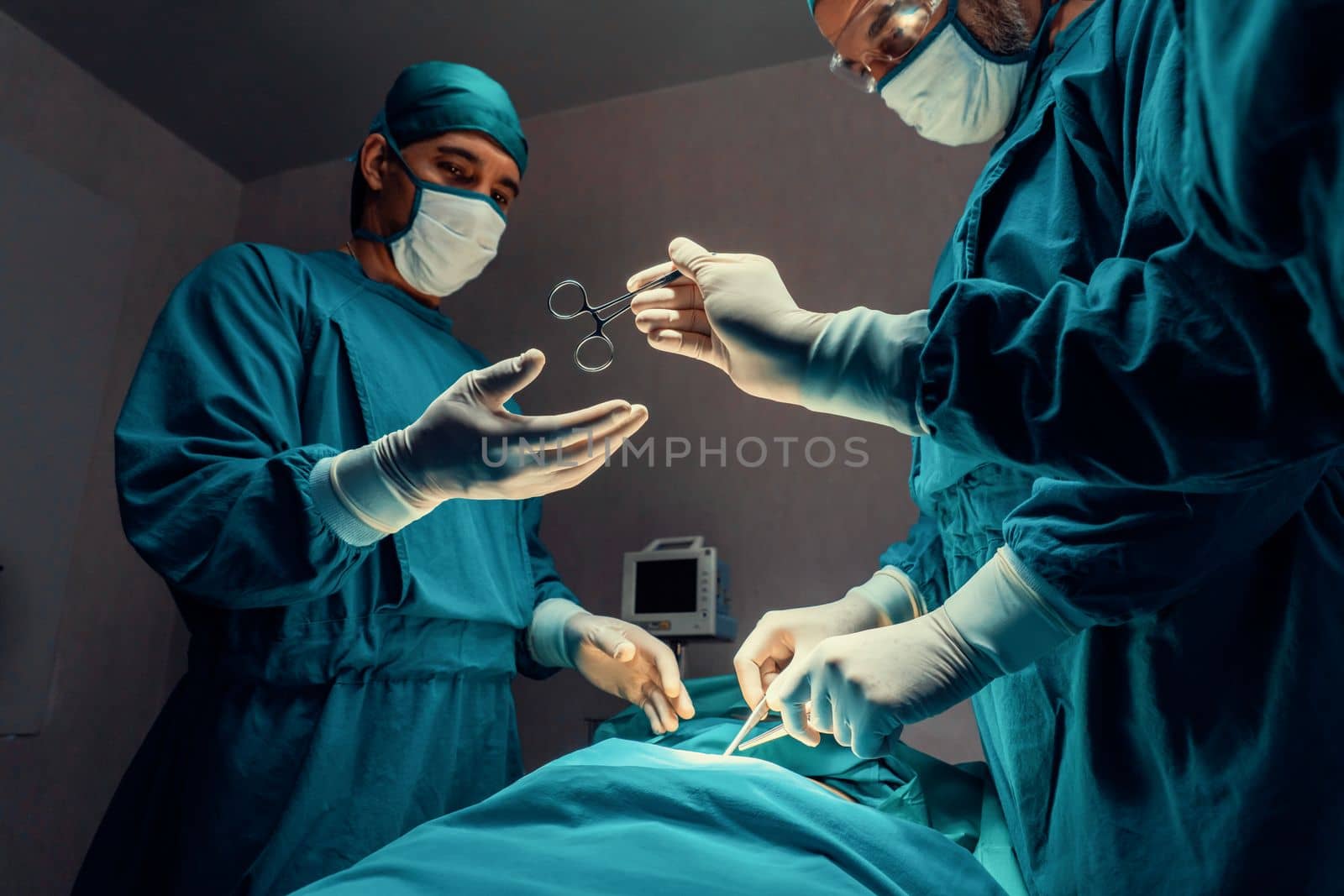 Surgical team performing surgery to patient in sterile operating room. In a surgery room lit by a lamp, a professional and confident surgical team provides medical care to an unconscious patient.