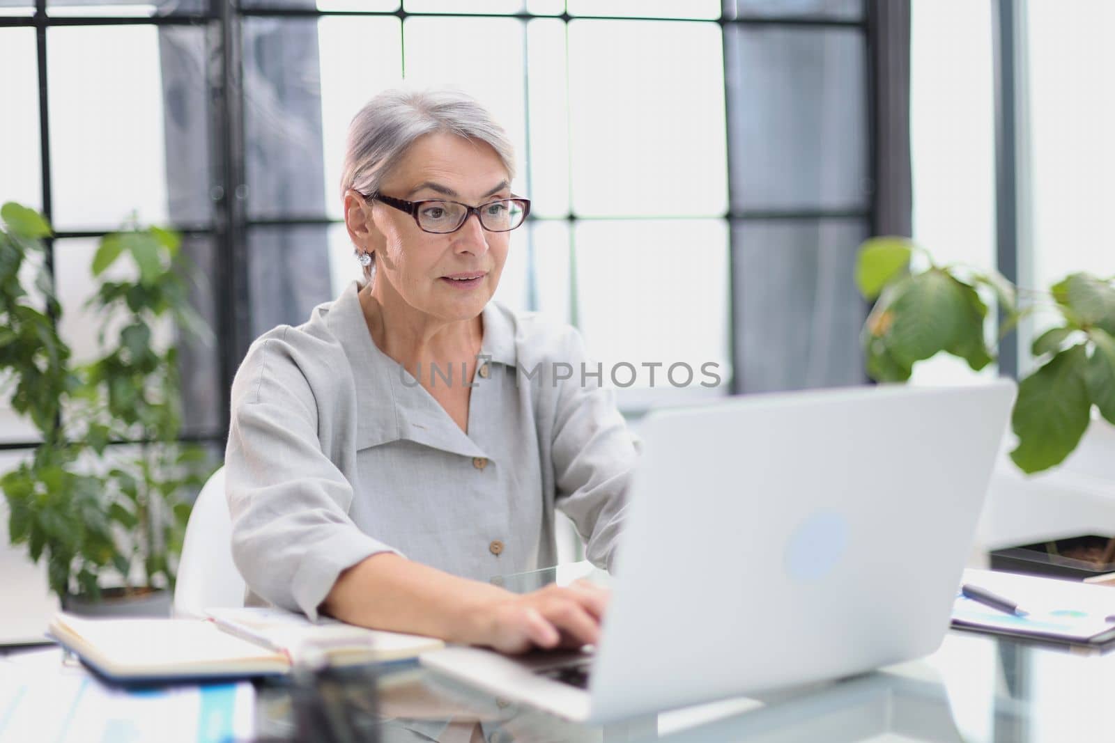 An elderly stylish woman working with a laptop in the office. by Prosto