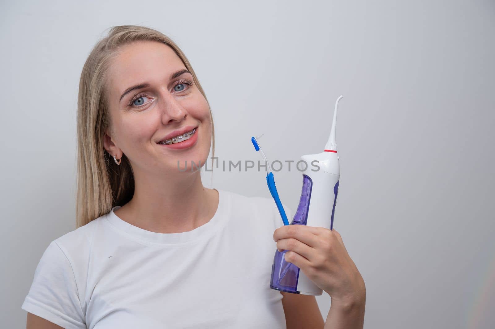 Smiling caucasian woman with braces on her teeth holding an irrigator and a toothbrush