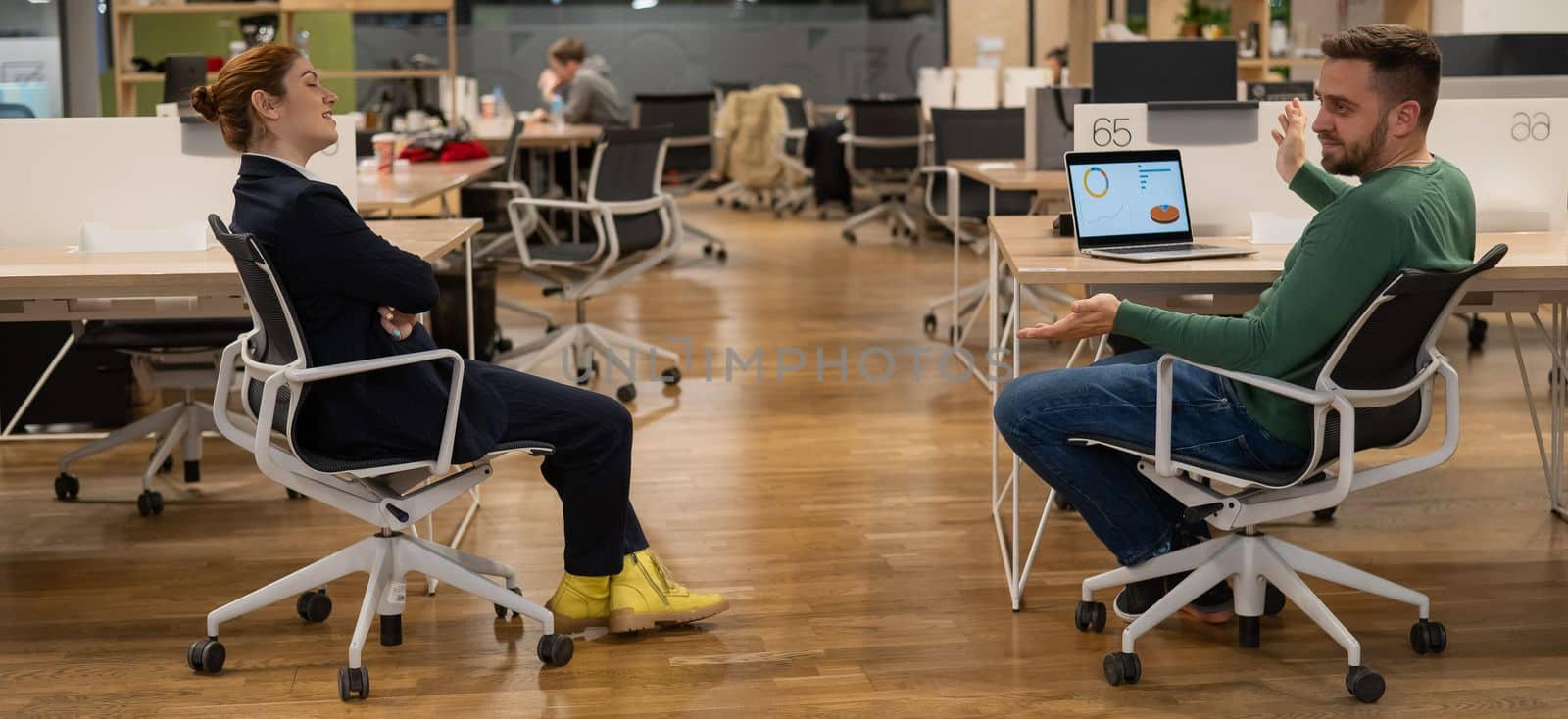 Redhead caucasian woman and bearded man are sitting on chairs in open space office