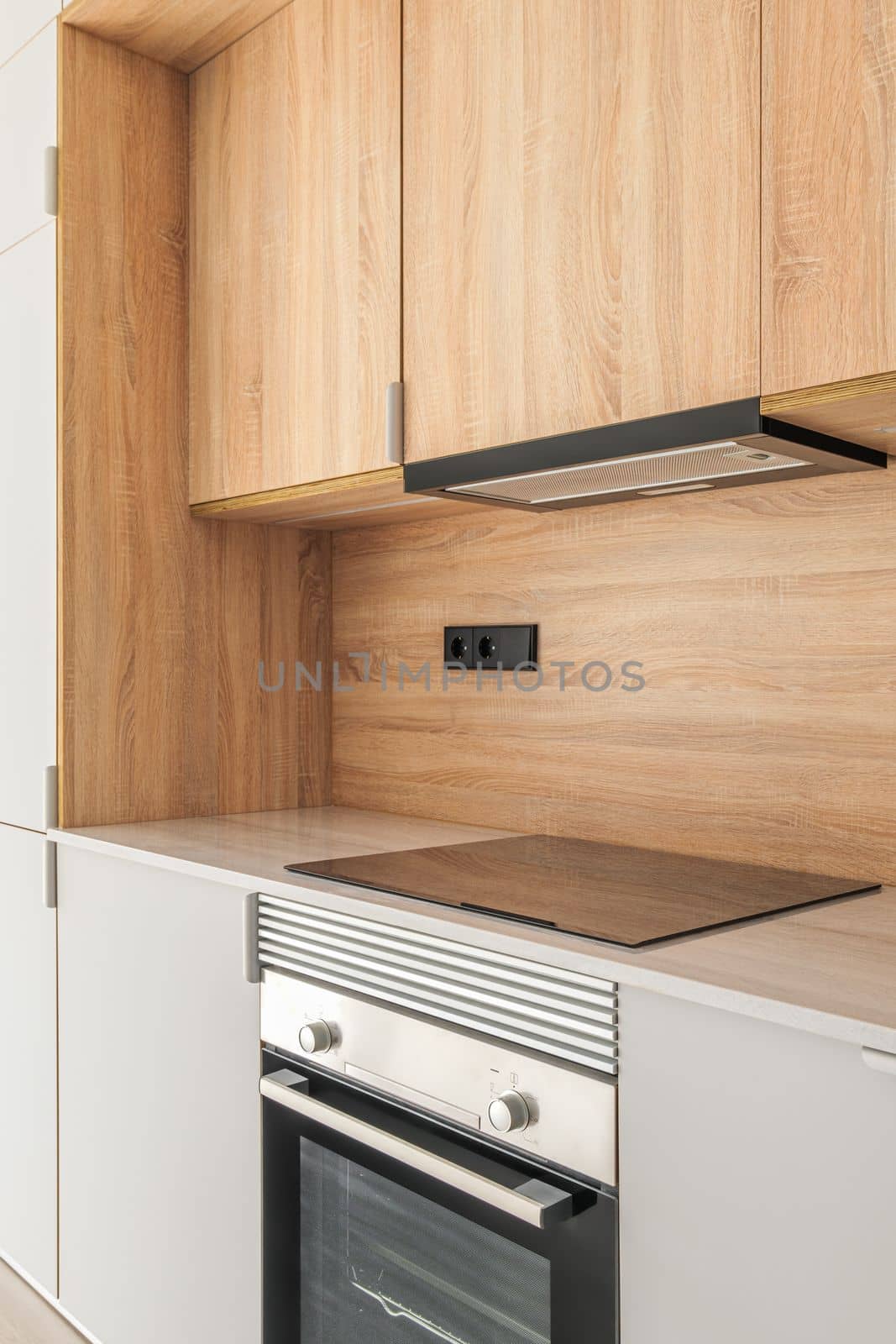 Closeup of piece of modular kitchen furniture made of wood. Modern cozy kitchen interior with appliances built into marble countertop. Hood hidden from view in cabinet above stove and oven