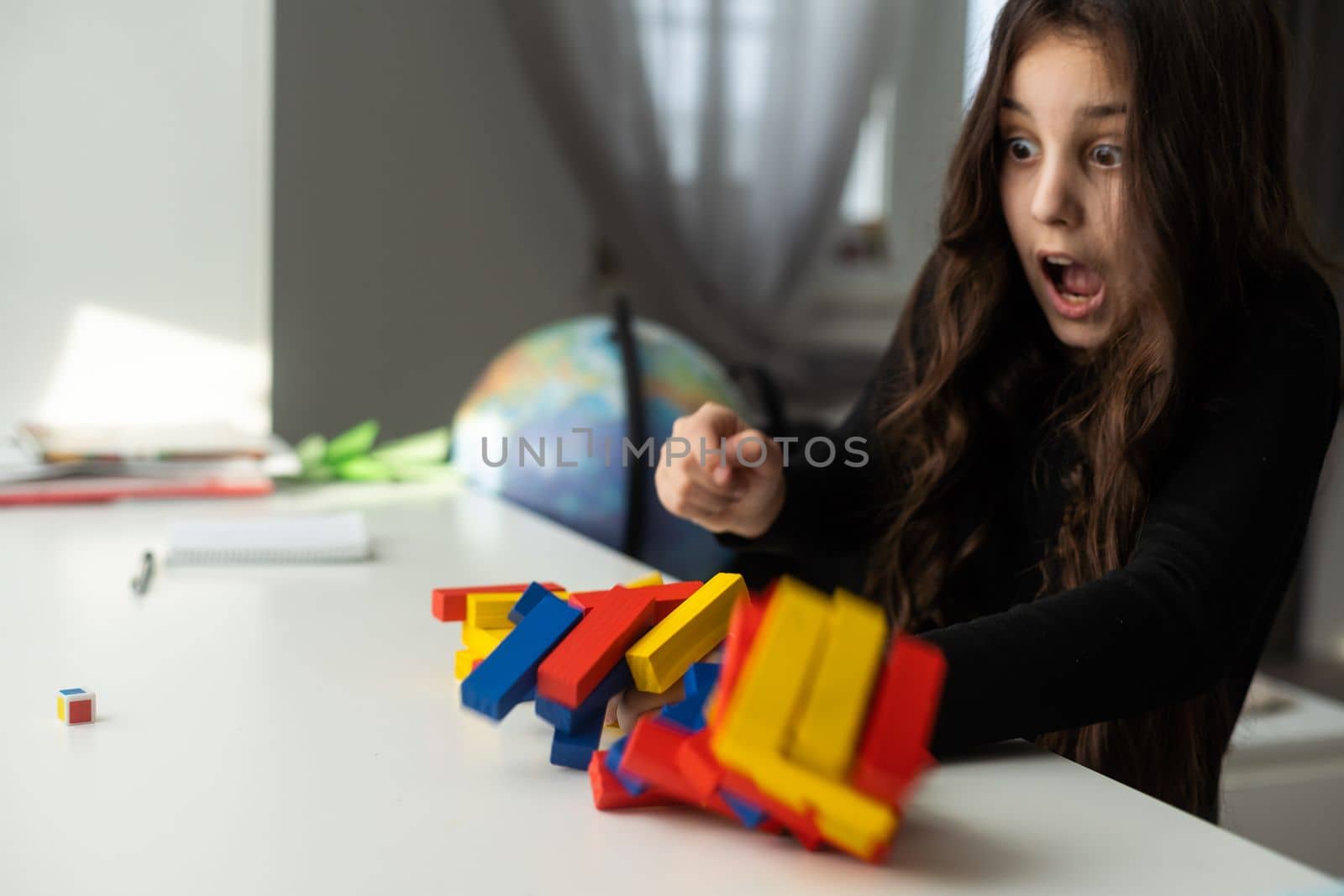 a little happy girl is playing the board game at the table. Construction of a tower made of wooden cubes by Andelov13
