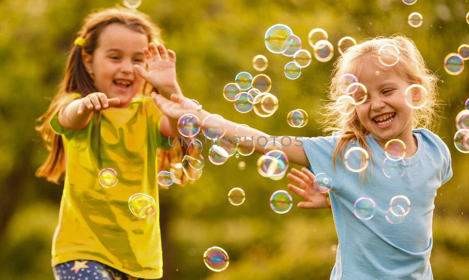 Two cheerful cute girls are playing outdoors with huge soap bubbles by Andelov13