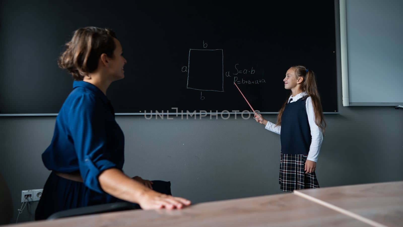 Caucasian little girl answers the question of the female teacher at the blackboard