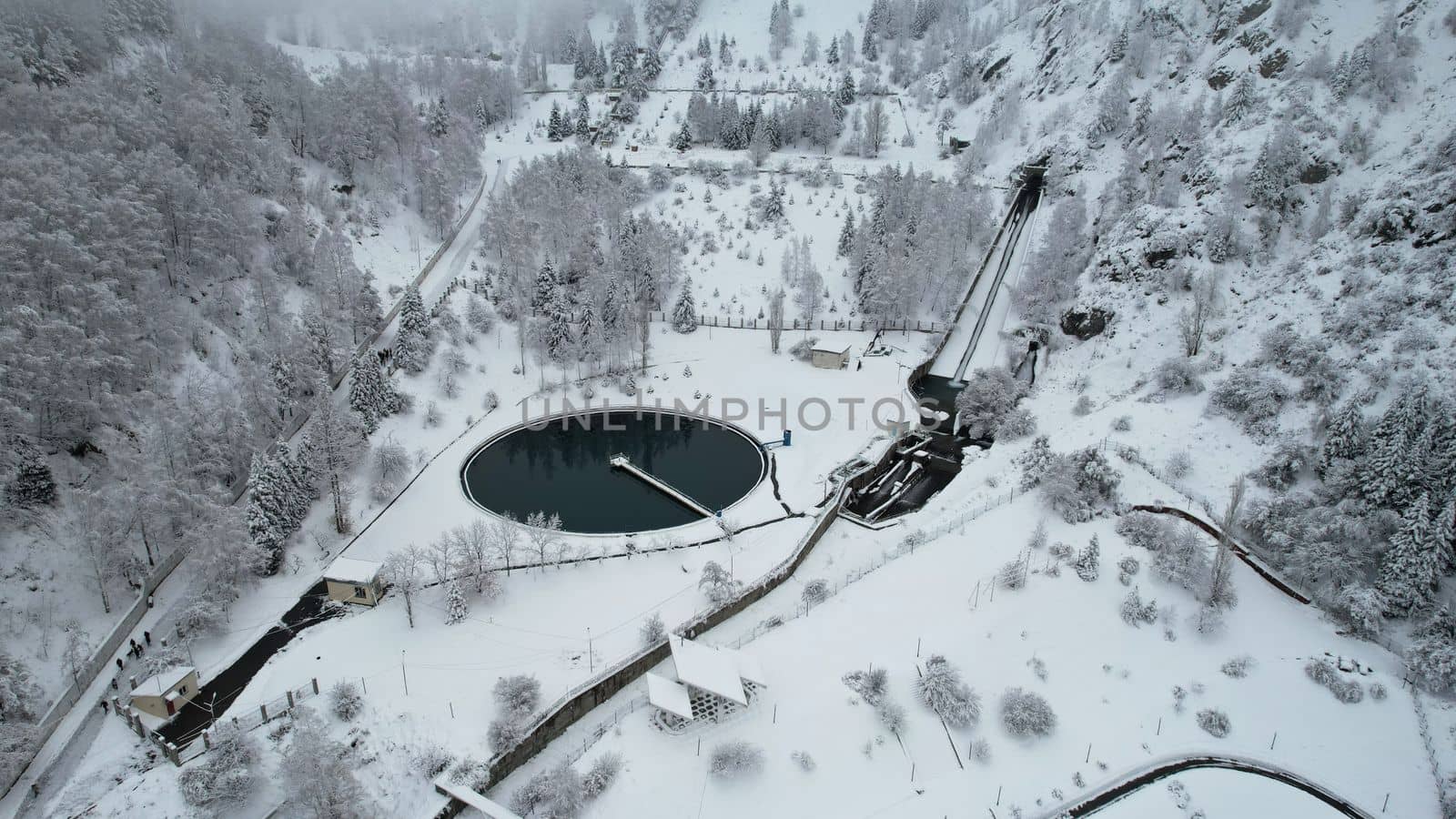 Snowy mountains with coniferous trees in Almaty. A reservoir for mountain water. Medeo Dam and the ladder of health. Everything is covered in clouds and snow. People and a cable car are visible