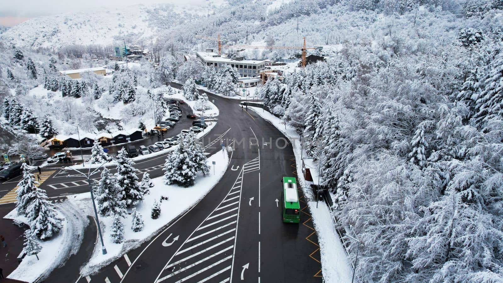 Snowy fairy-tale road in a mountain forest. Christmas or New Year has come. Coniferous trees in the snow. There is a green bus, people are walking. Light fog. The view from the drone. Medeo, Almaty