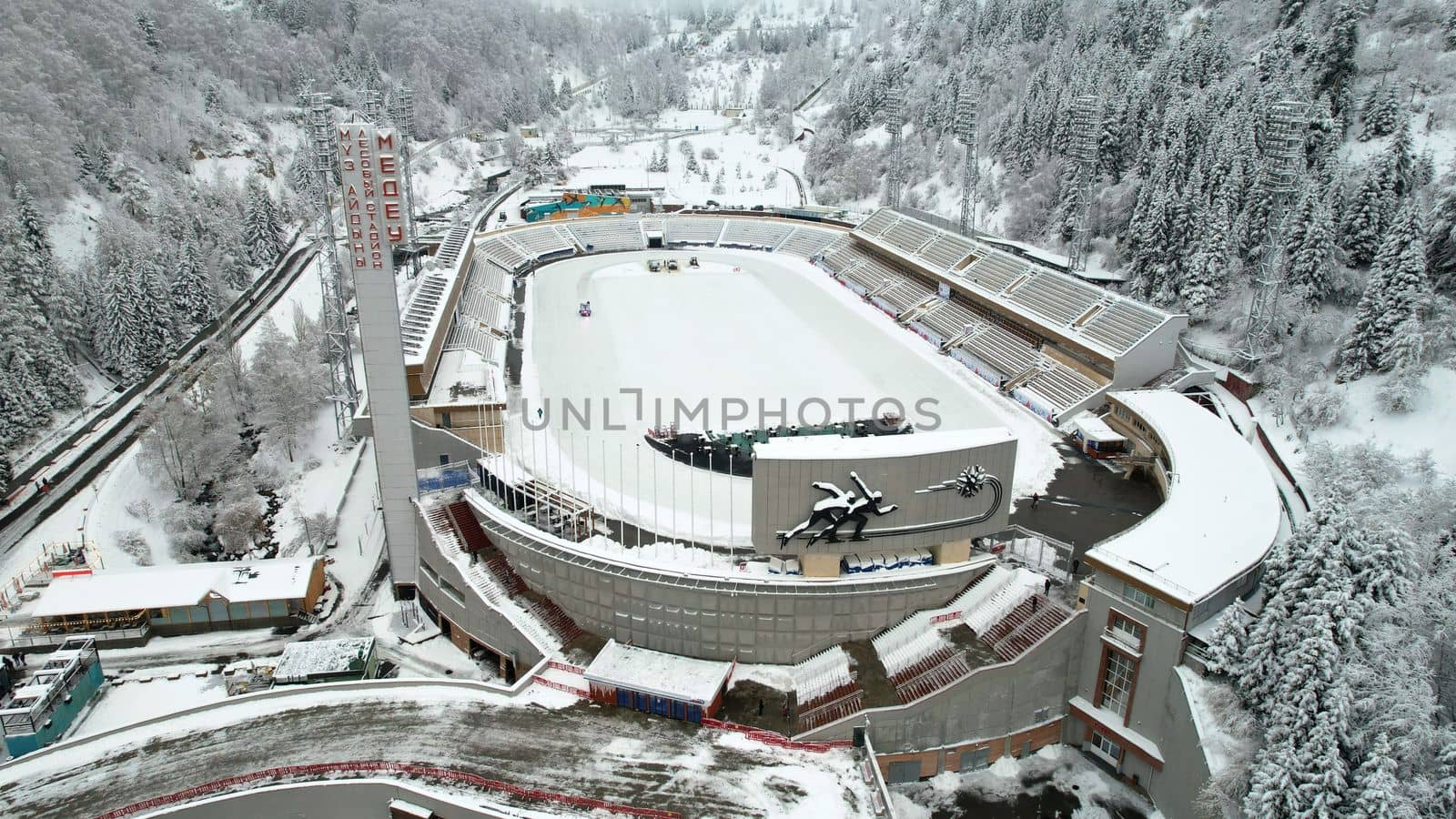 Winter alpine skating rink Medeo in the mountains. Drone view of the snowy forest and mountains. White clouds and fog in the gorge. Snow removal is underway. A large stadium. Almaty, Kazakhstan