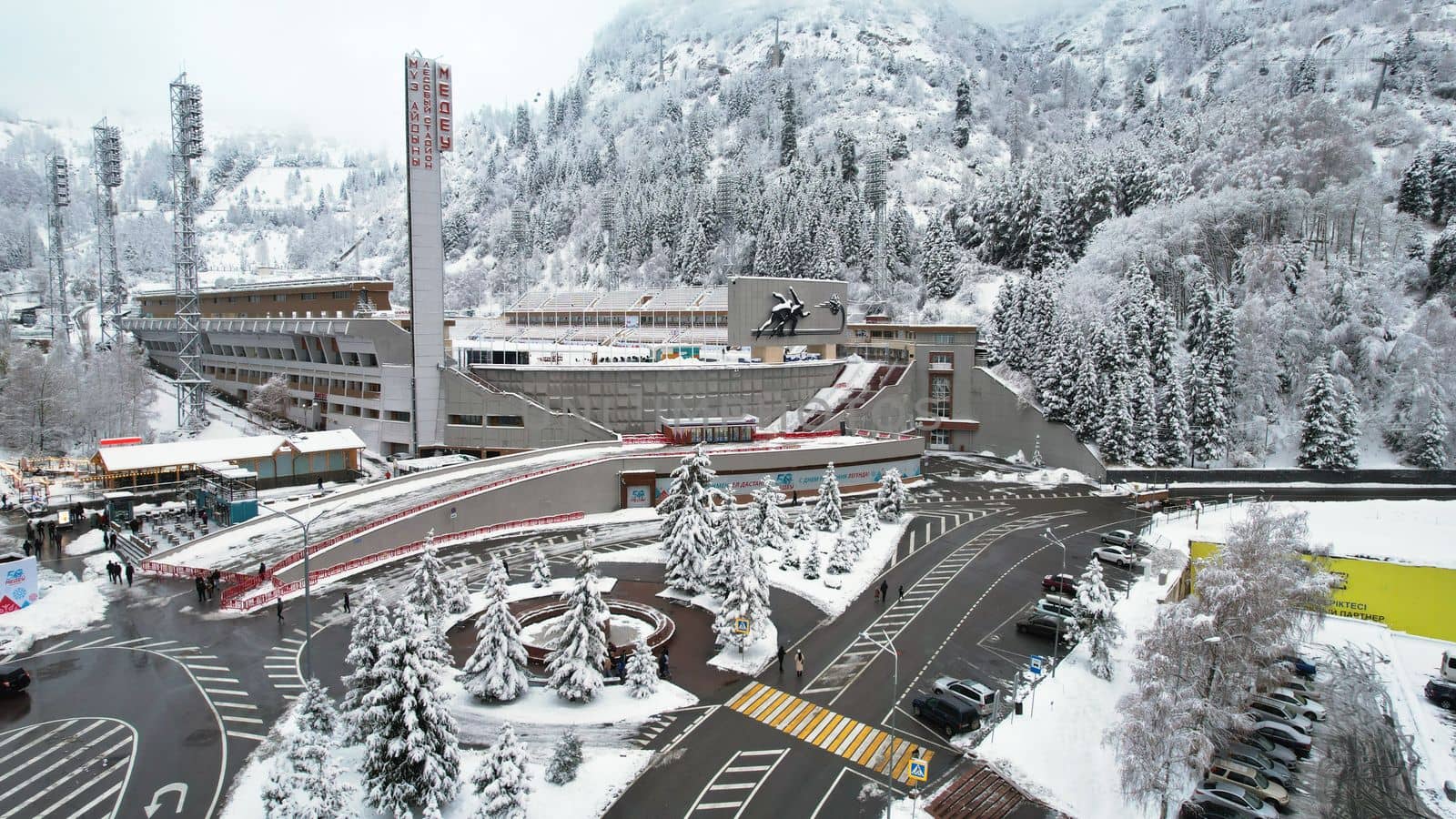 Winter alpine skating rink Medeo in the mountains. Drone view of the snowy forest and mountains. White clouds and fog in the gorge. Snow removal is underway. A large stadium. Almaty, Kazakhstan