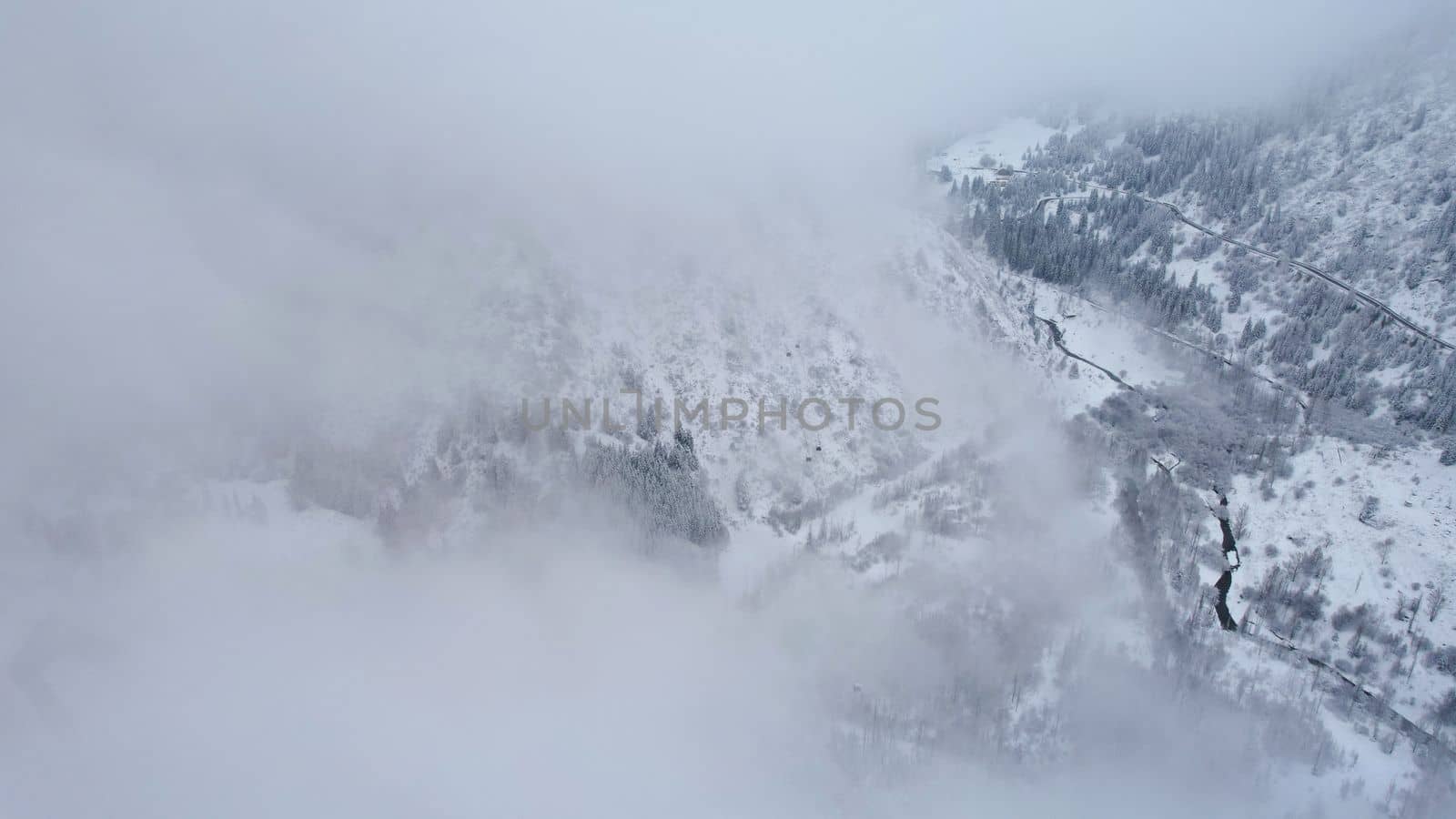 Snowy mountains with coniferous trees in the clouds. Medeo Dam. Everything is in fog and snow. Christmas and New Year have come. Aerial view from the drone on road, dam and trees. Almaty, Kazakhstan