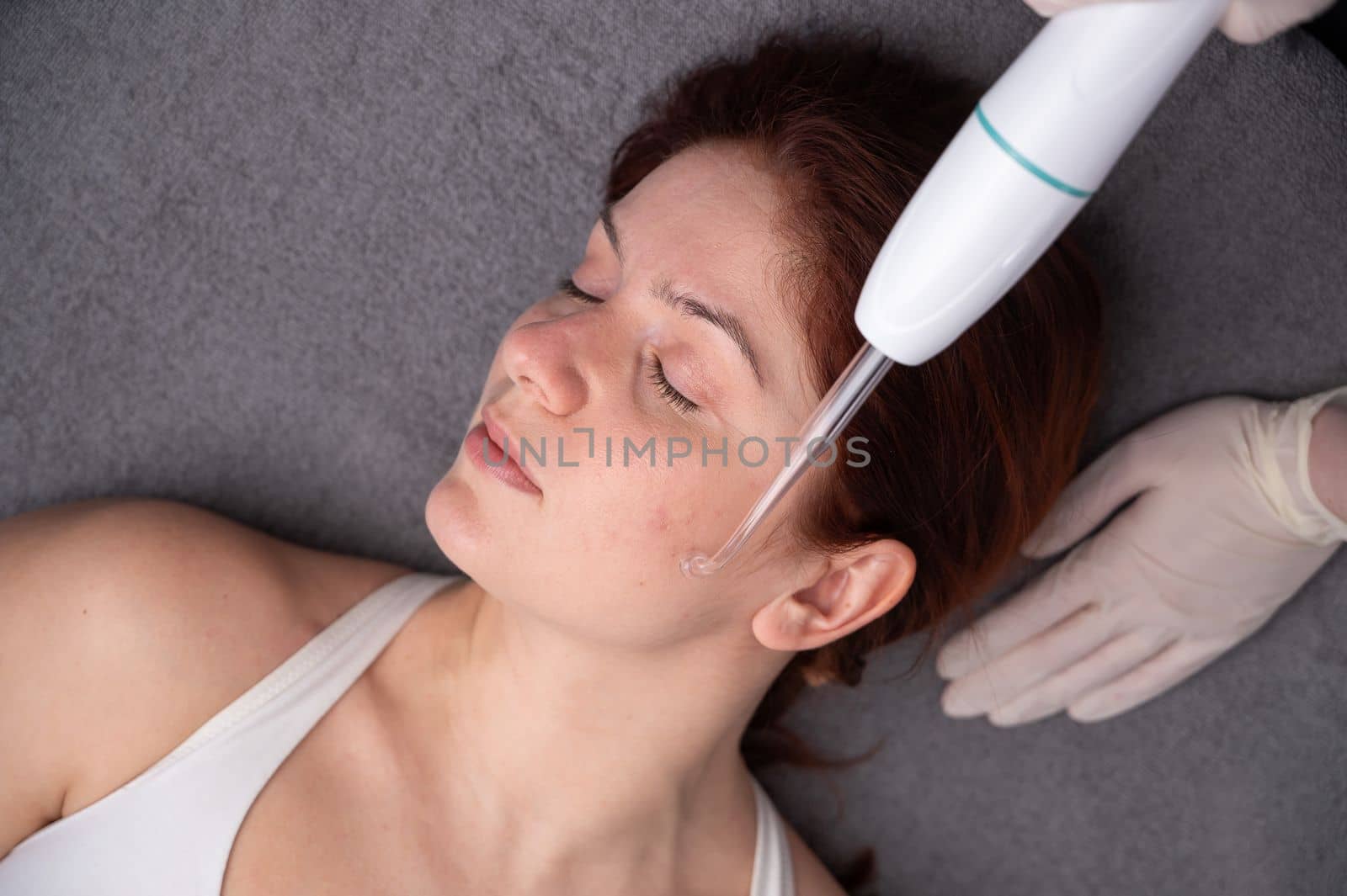 The doctor uses the darsonval apparatus against acne on the face of a female patient