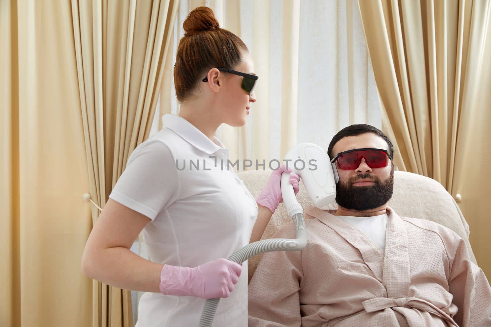 Bearded man getting laser facial treatment by professional cosmetologist in a beauty clinic. Healthy man lifestyle concept