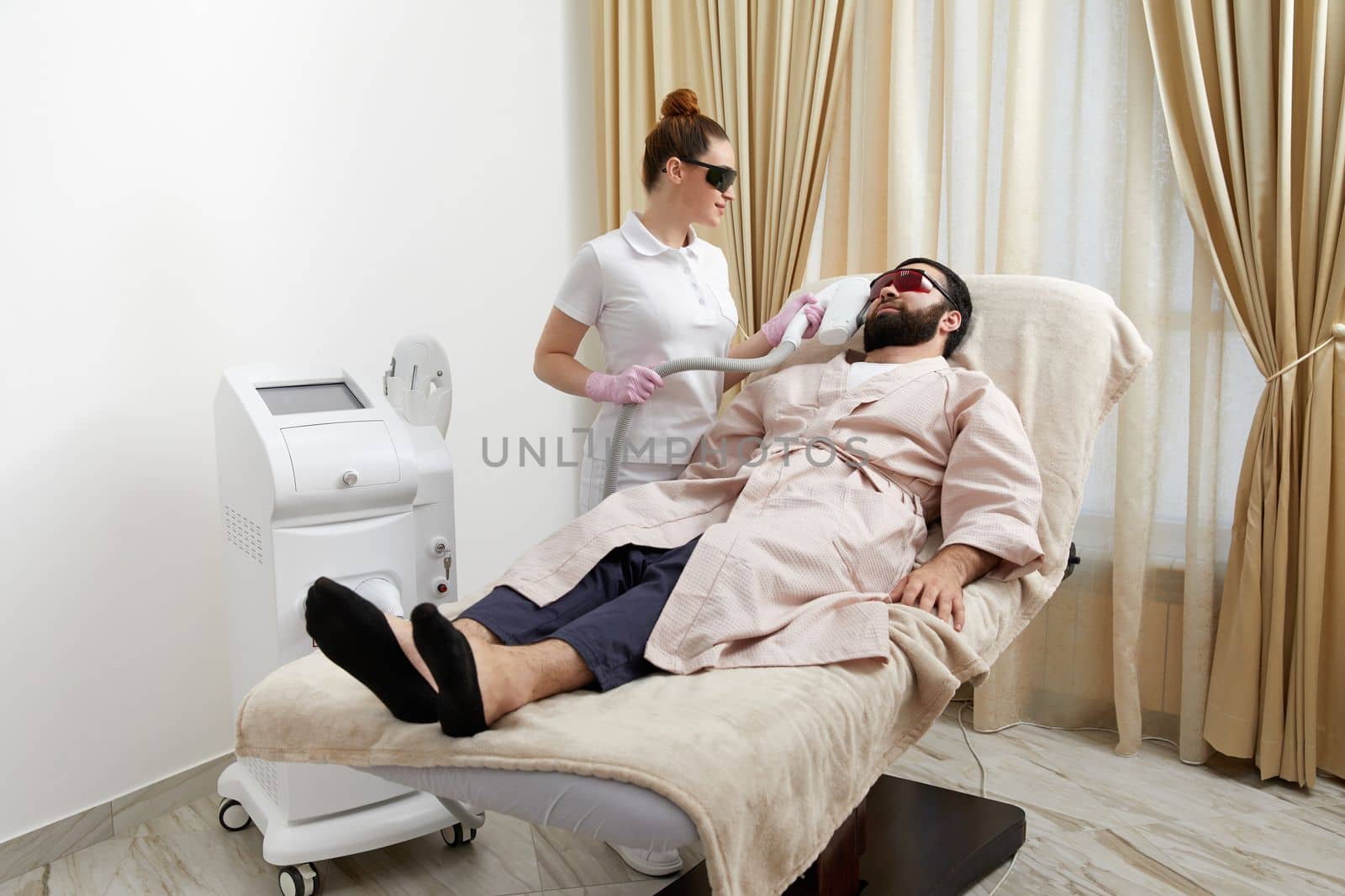 Bearded man getting laser facial treatment by professional cosmetologist in a beauty clinic by Mariakray