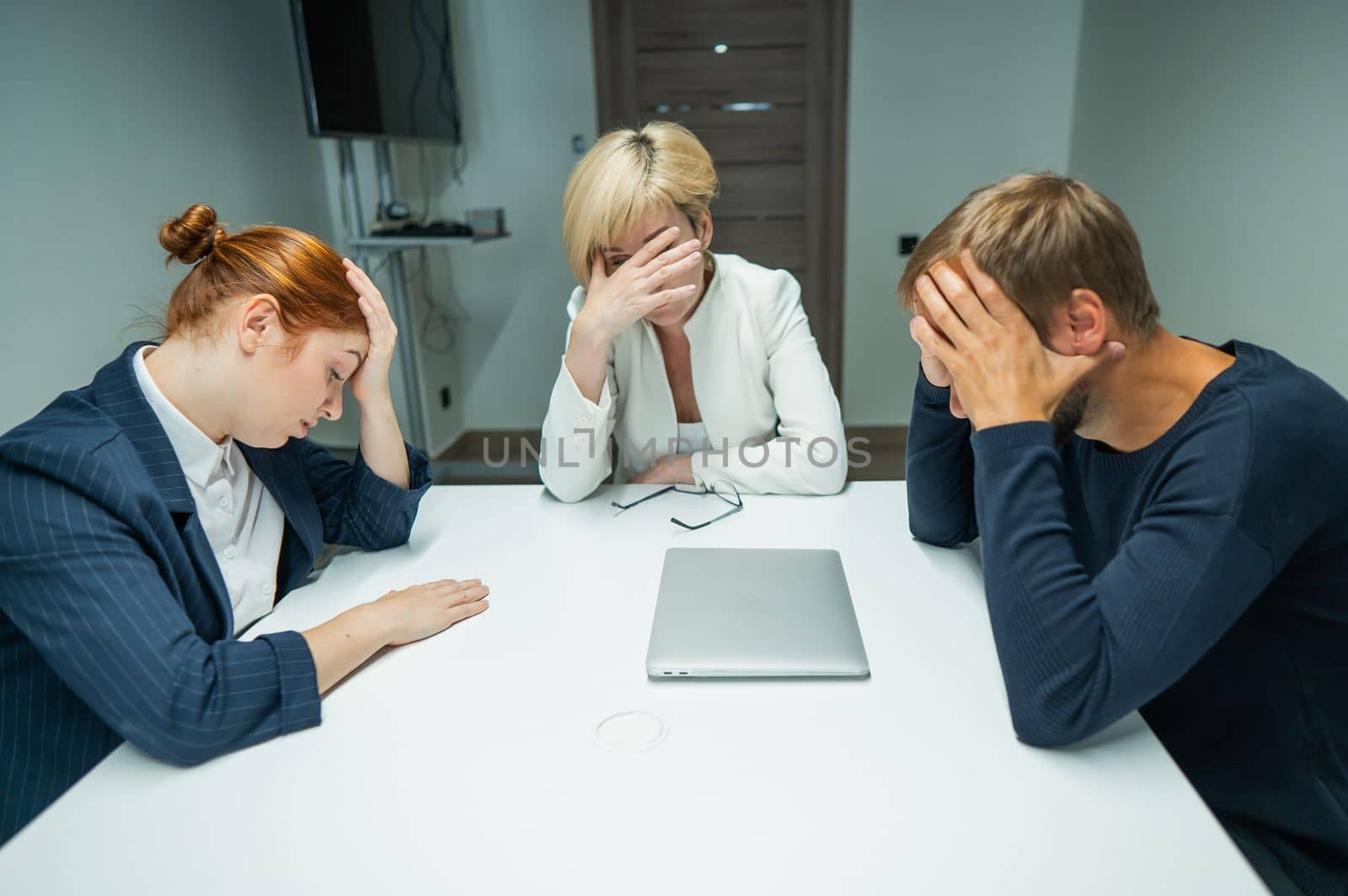 Blond, red-haired woman and bearded man in suits in the office.Colleagues sit at a table in a conference room and hold their heads in thought. by mrwed54