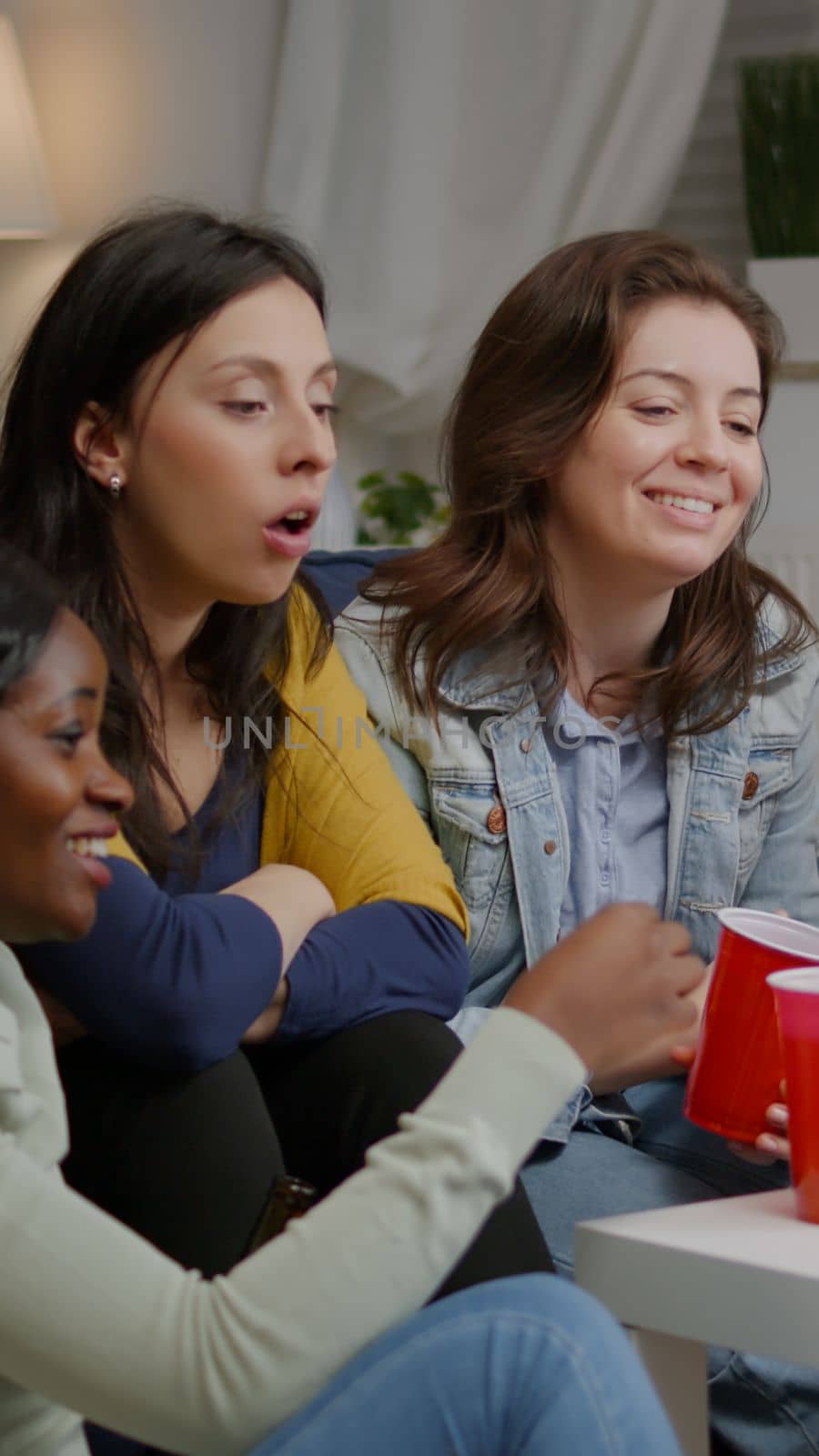 Multiethnic friends sitting on couch having online videocall meeting socialising with virtual collegue using laptop. Group of mixed race people having fun together late at night in living room